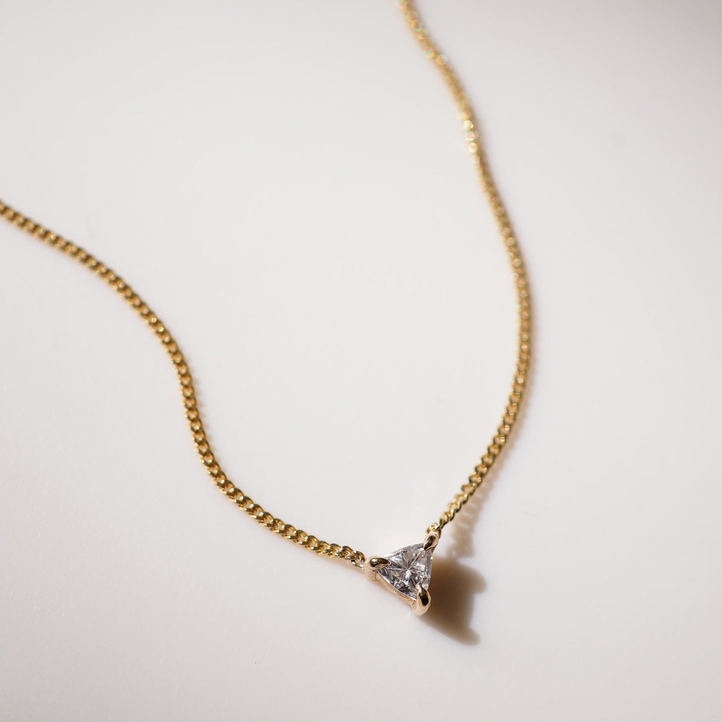 Gold necklace with a triangular pendant on a light background