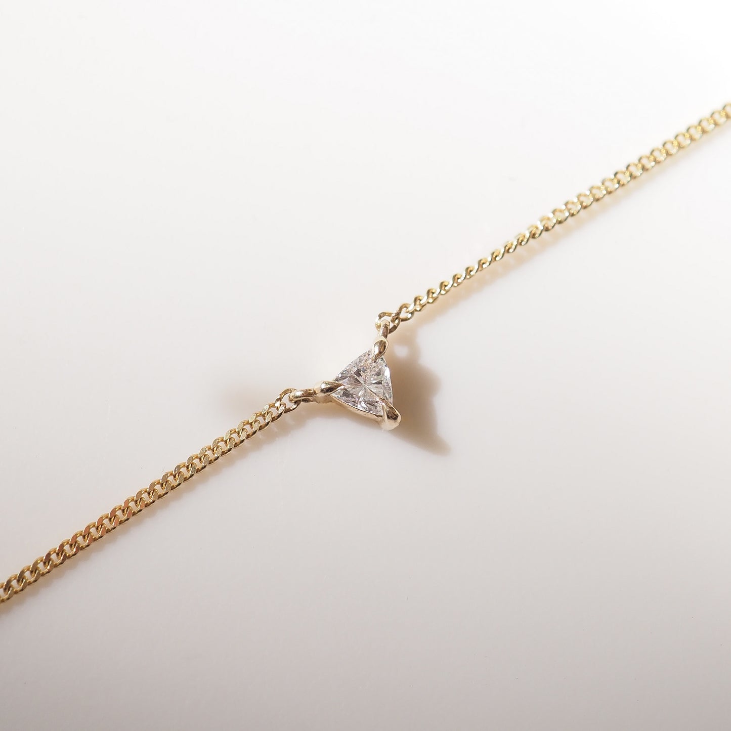 Gold necklace with a triangle-shaped diamond pendant on a light background