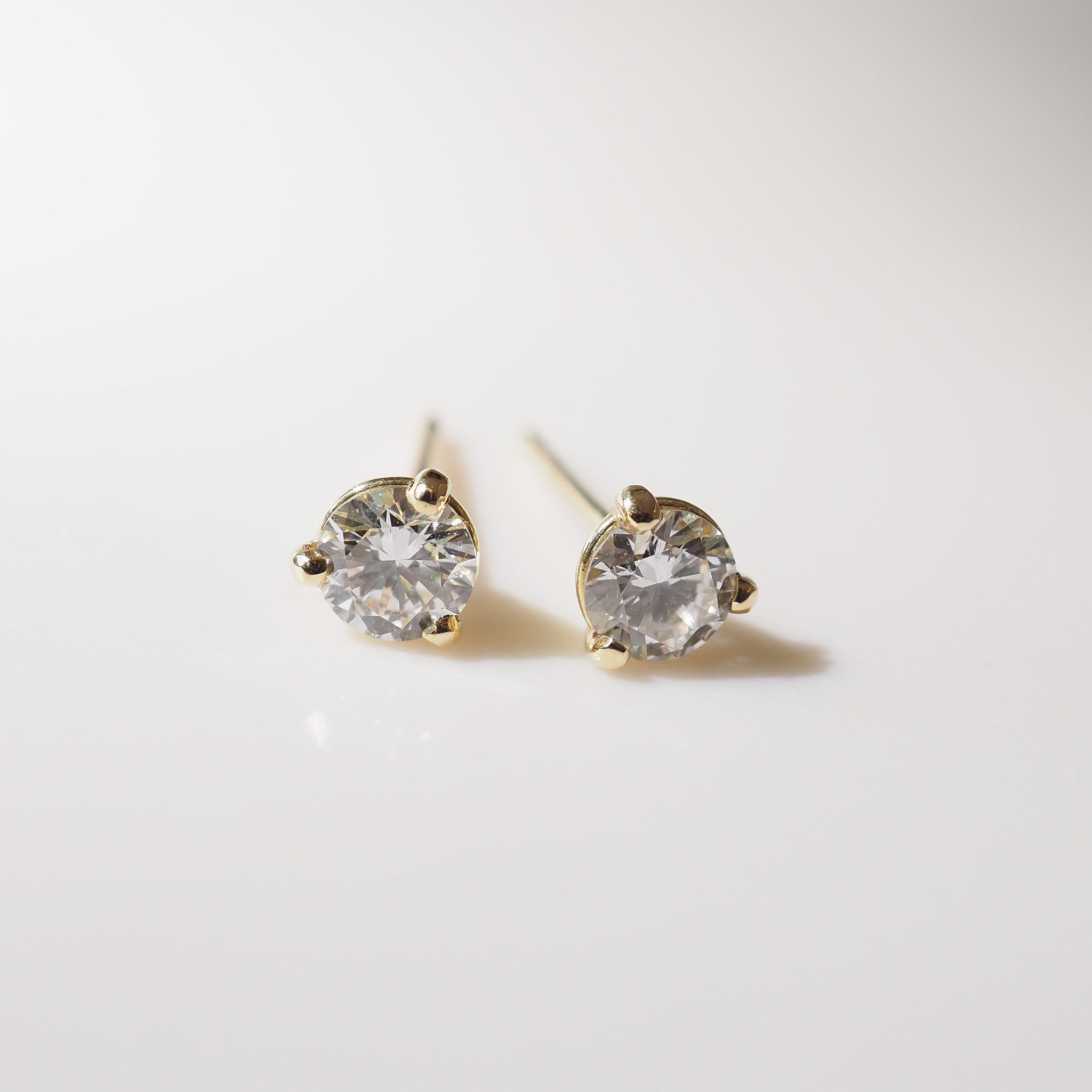 Pair of gold stud earrings with clear gemstones on a light gray background