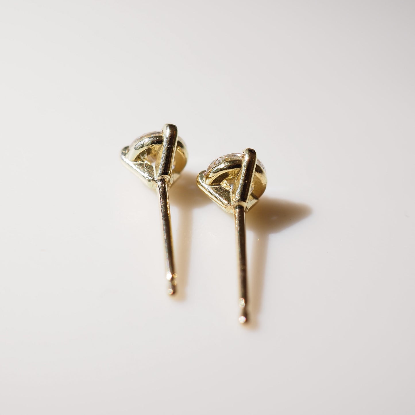 Gold earrings with diamond-like tops on a light background