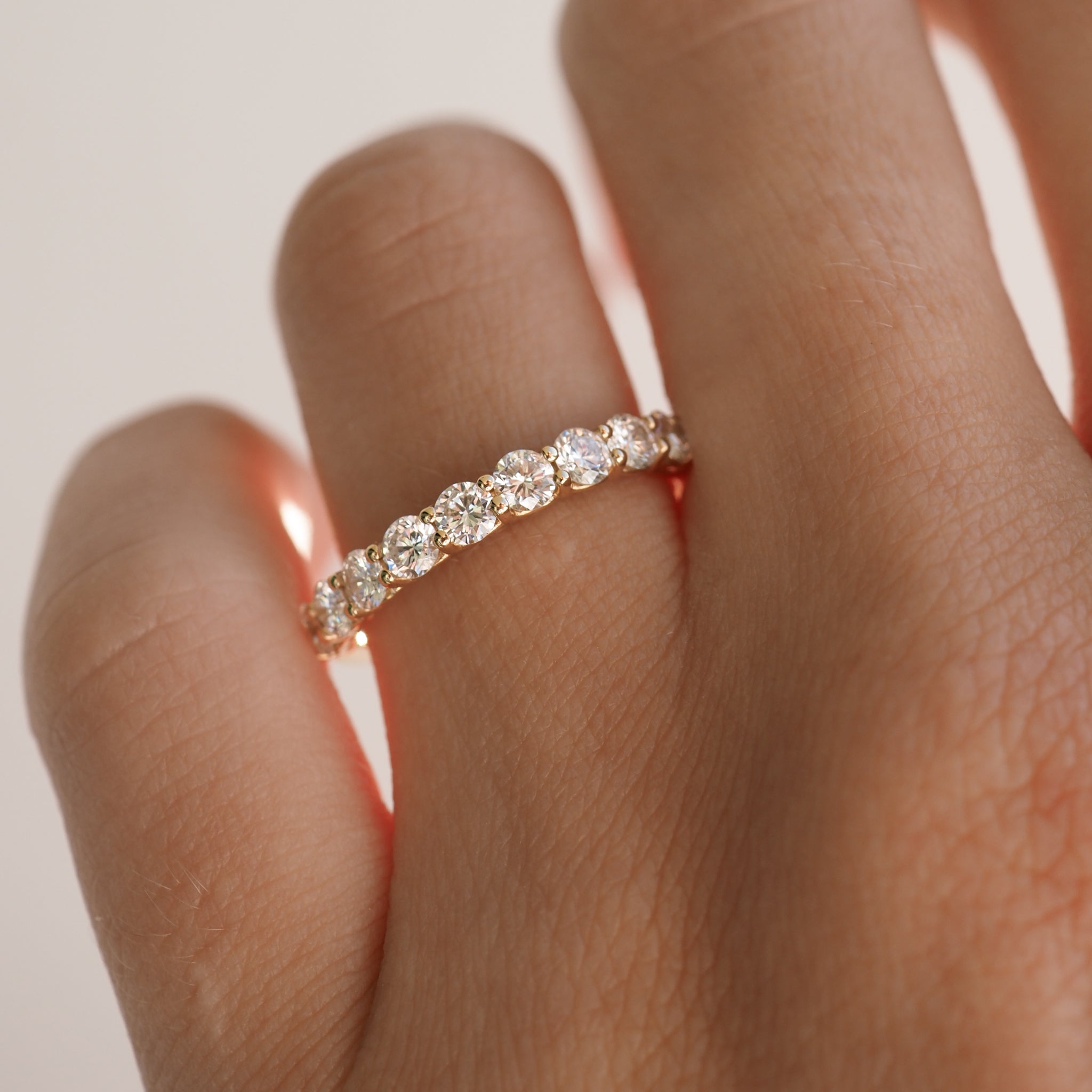 A hand wearing an elegant gold eternity band set with round-cut diamonds, showcasing luxury jewellery craftsmanship.