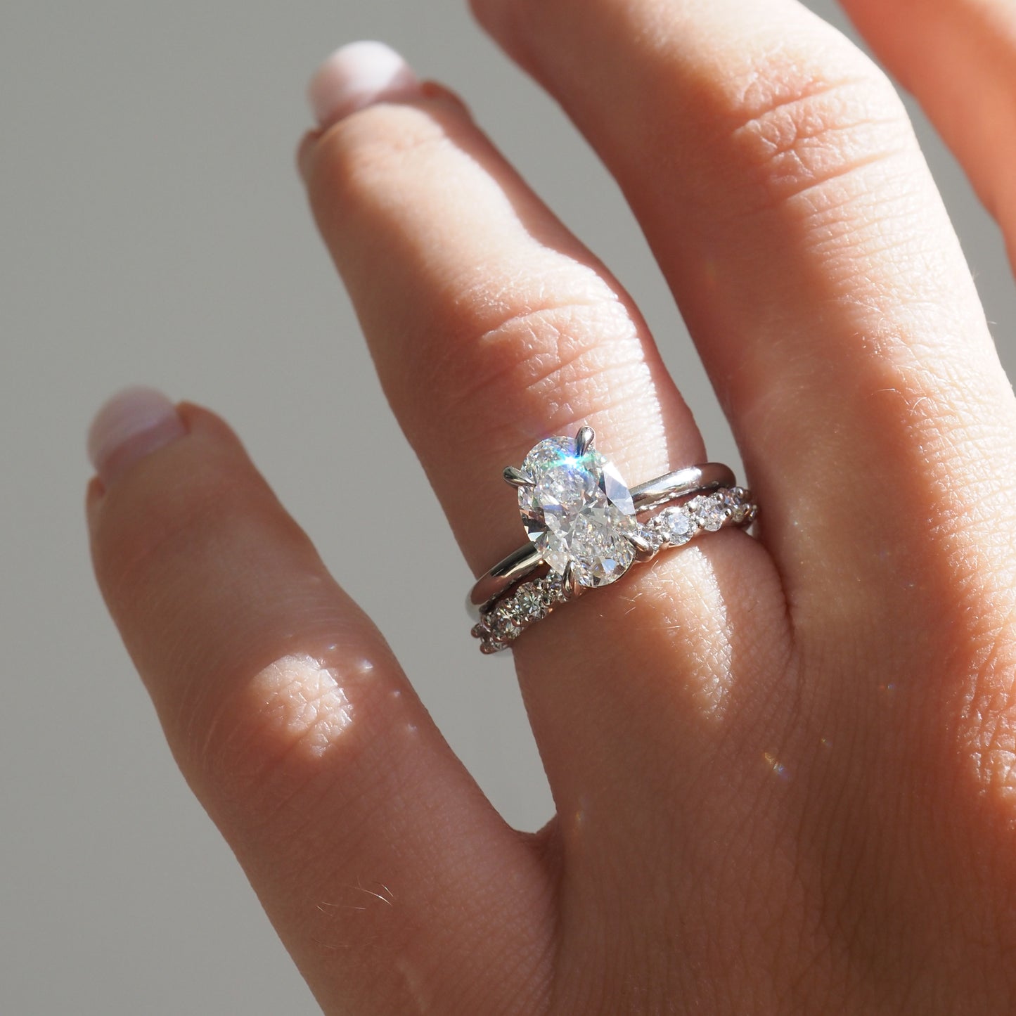 Close-up of a hand with a luxury engagement ring set, featuring a large oval-cut diamond and sparkling band in natural light, showcasing high-end jewellery.