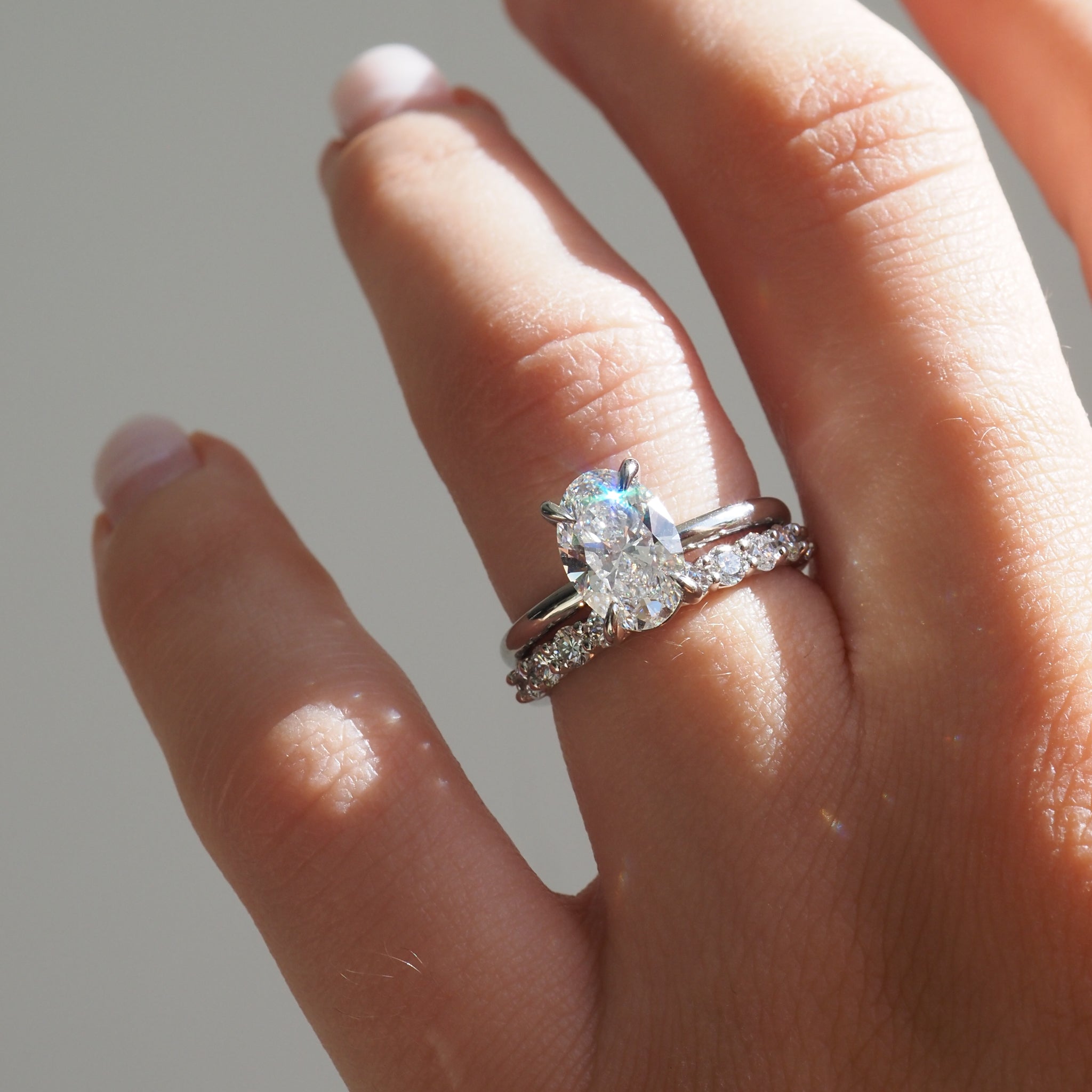 Close-up of a hand with a luxury engagement ring set, featuring a large oval-cut diamond and sparkling band in natural light, showcasing high-end jewellery.
