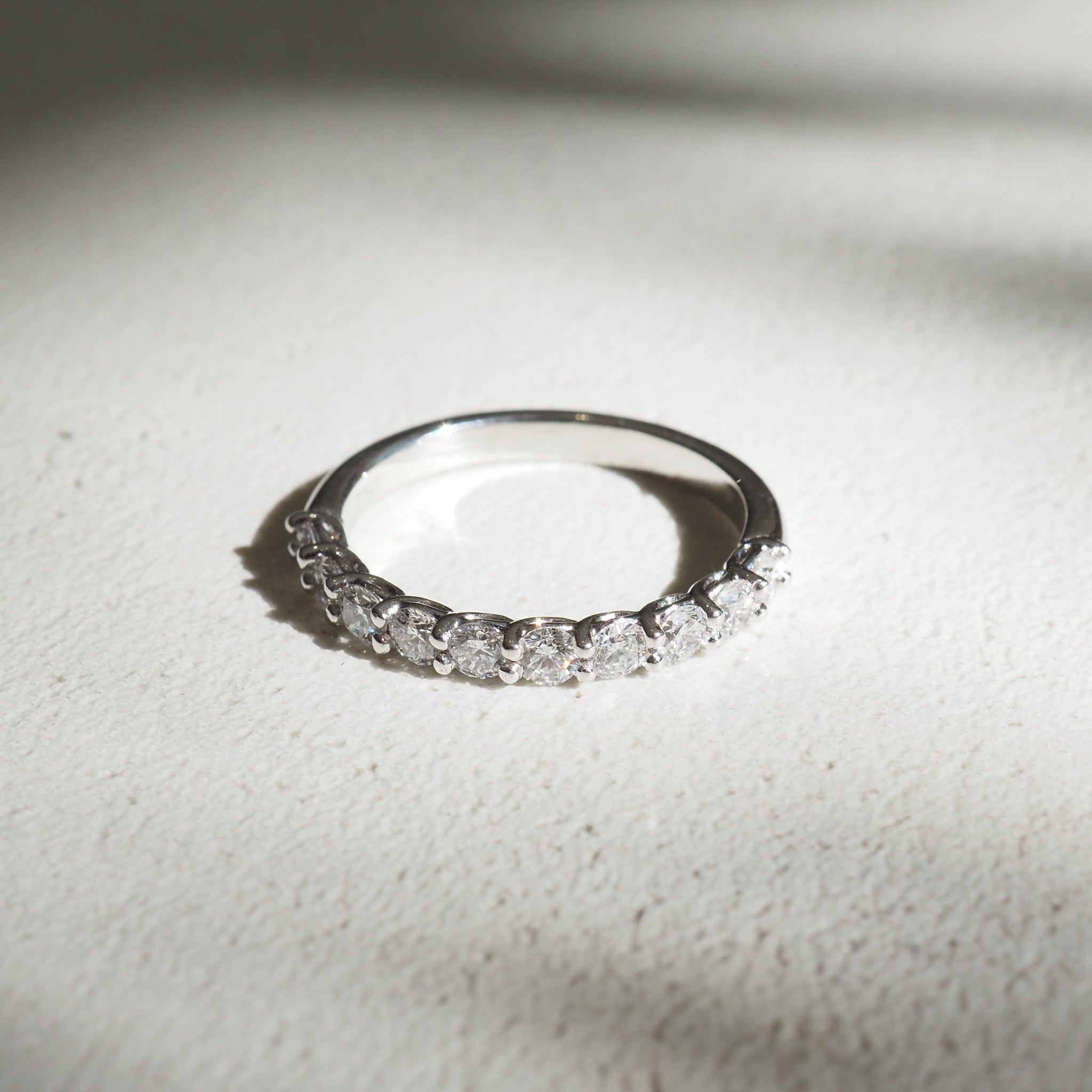 Elegant diamond eternity ring with a sleek silver band, beautifully illuminated, casting subtle shadows on a light textured surface.