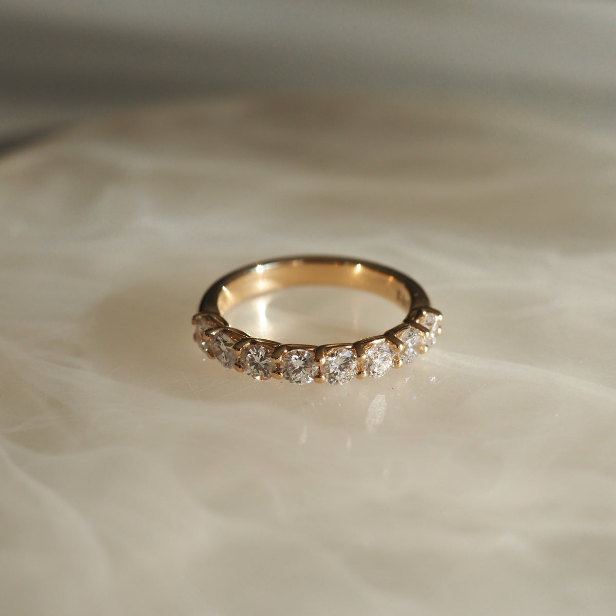 Gold ring with round brilliant diamonds set in a row, displayed on a soft, light-coloured surface.