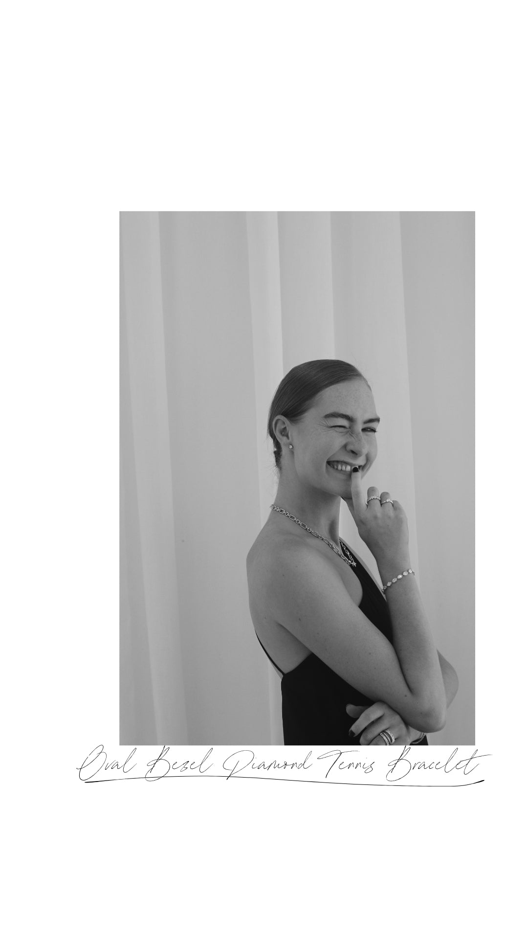 Smiling woman in a black dress, wearing an elegant diamond tennis bracelet and necklace, standing against a neutral background.