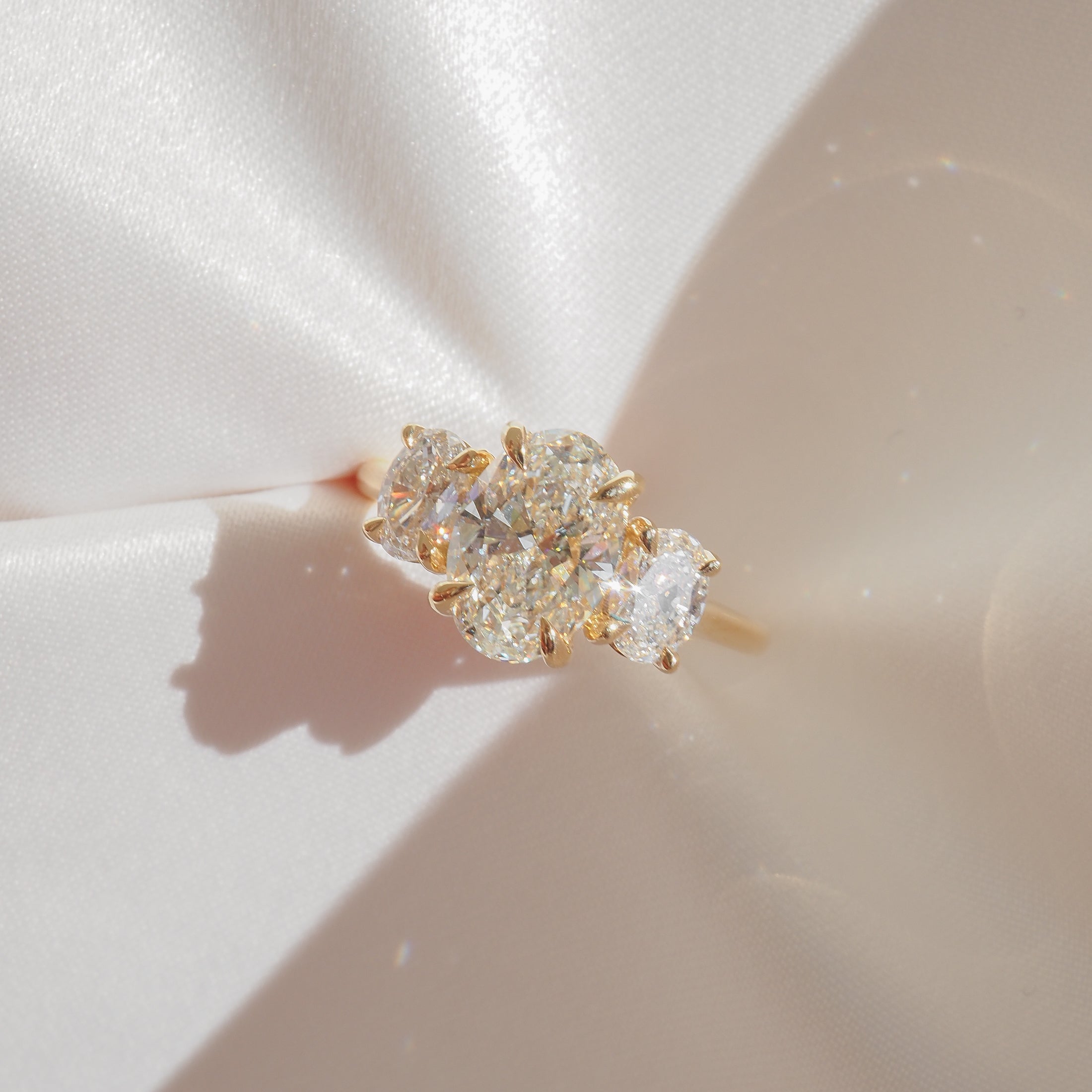 Gold ring with three sparkling diamond stones on a soft, satin background. Luxurious jewellery piece, perfect for weddings or special occasions.