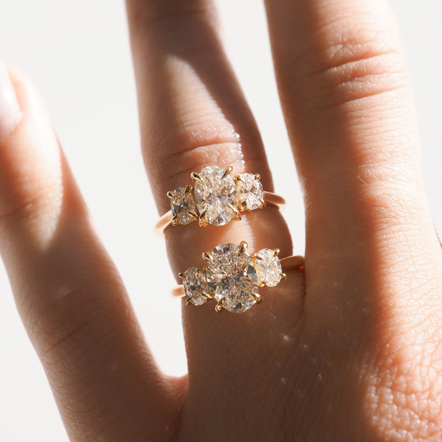 Hand wearing two gold rings with large, sparkling diamonds in sunlight. High-end luxury jewellery showcasing elegance and sophistication.