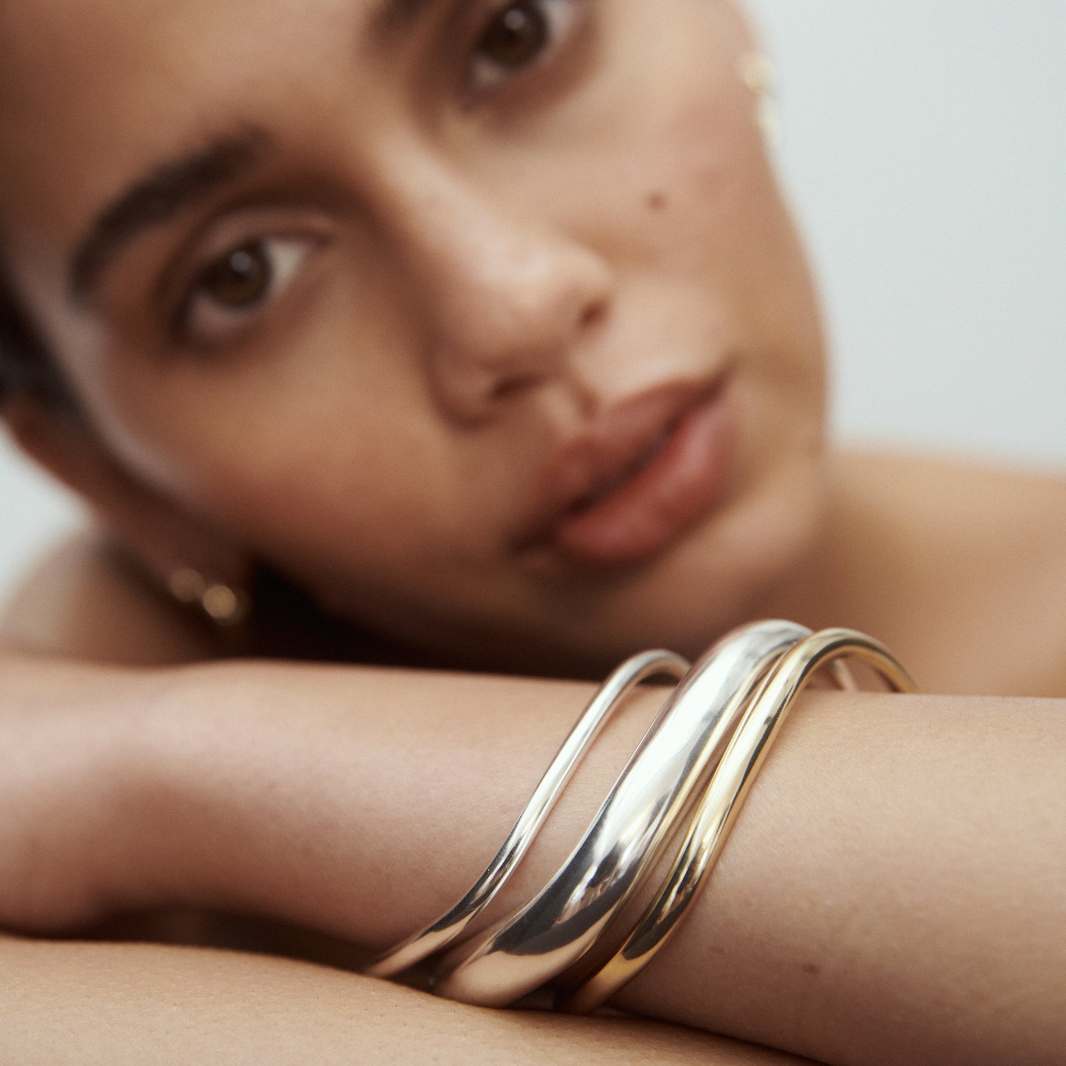 Close-up of a woman resting her head on her arm, showcasing sleek, interwoven silver and gold high-end bangles, adding a touch of luxury.