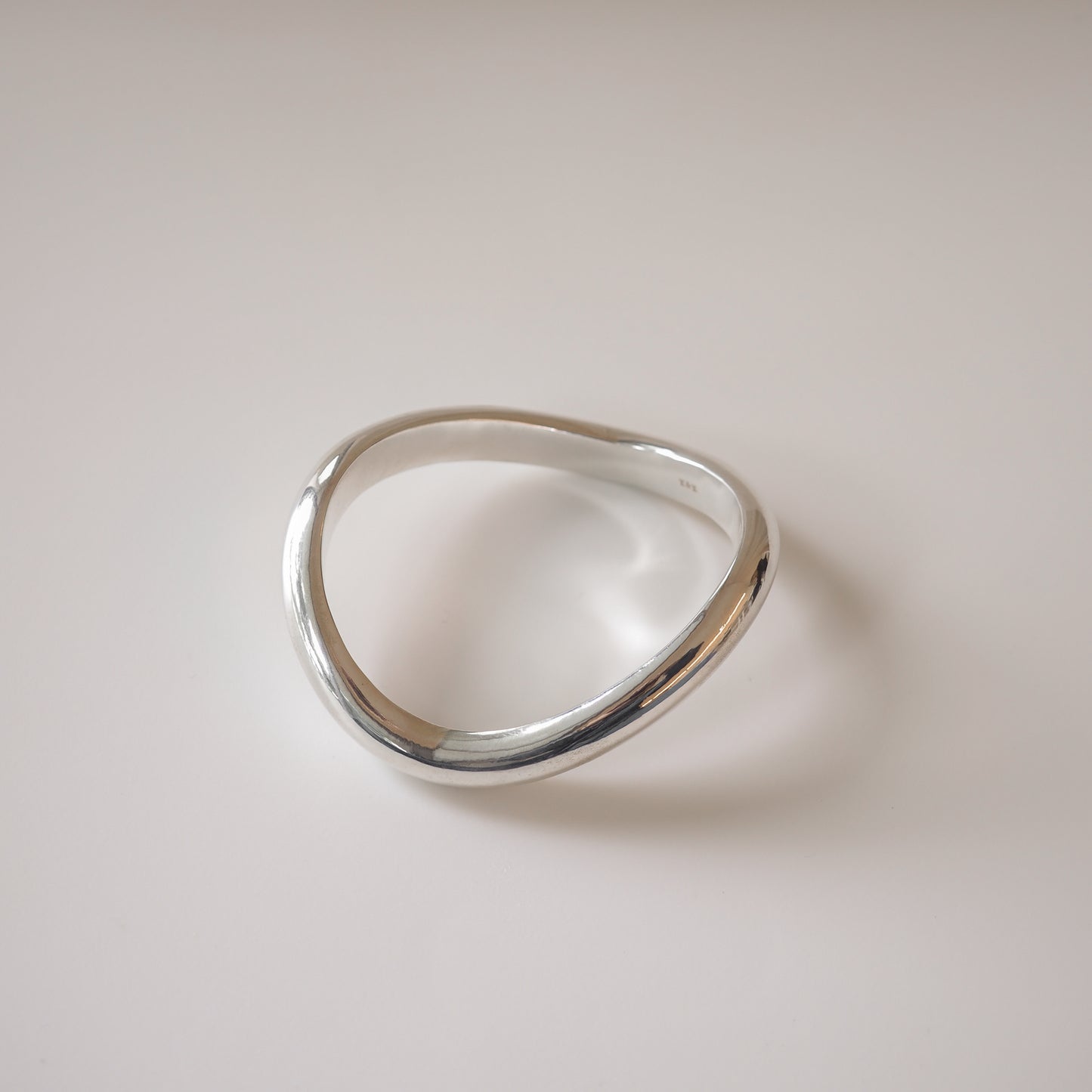 Sculptural silver bangle with a fluid, asymmetrical design on a neutral background, showcasing luxury jewellery elegance.