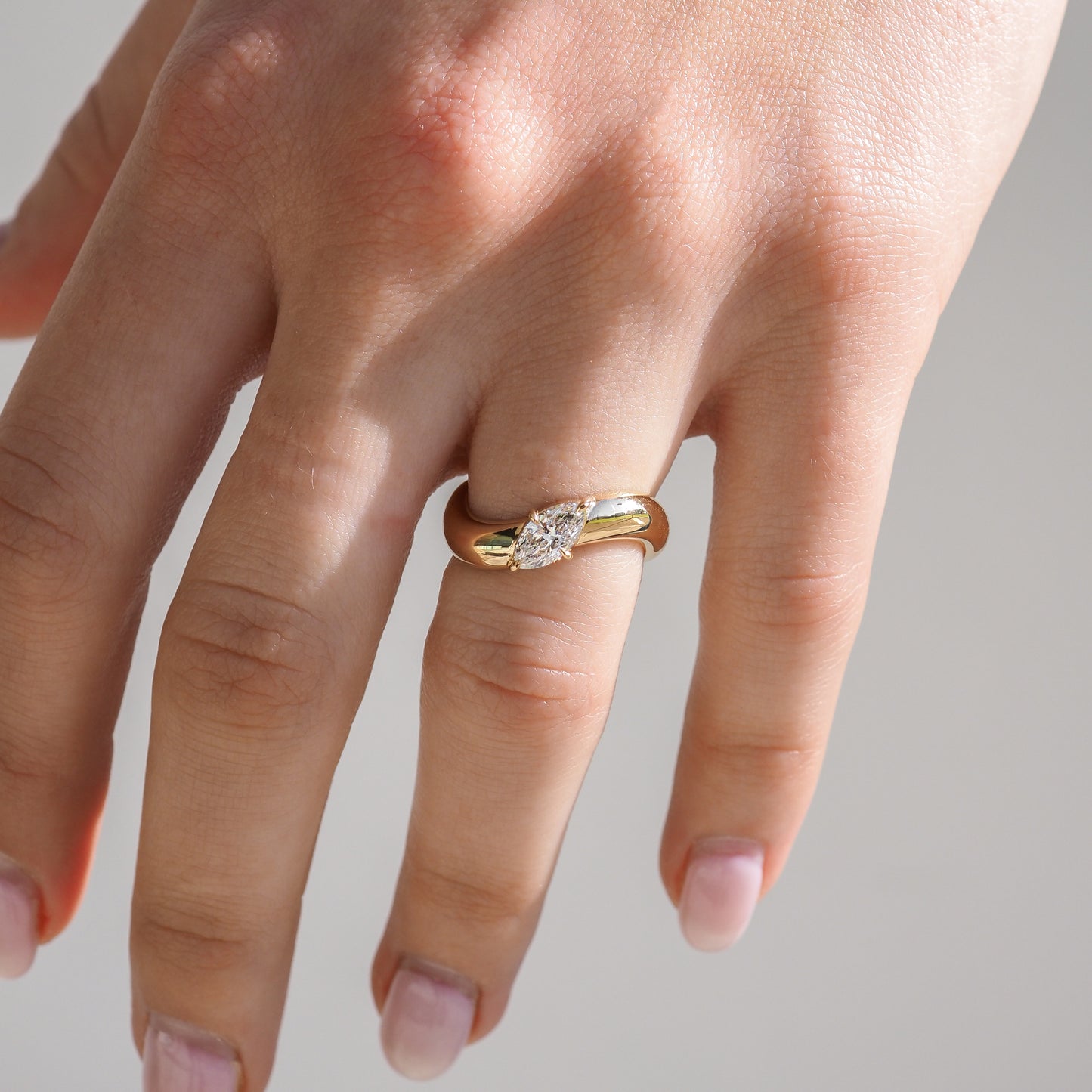 A hand wearing an elegant gold ring with a single, prominent diamond set in the centre, showcasing luxury jewellery design.