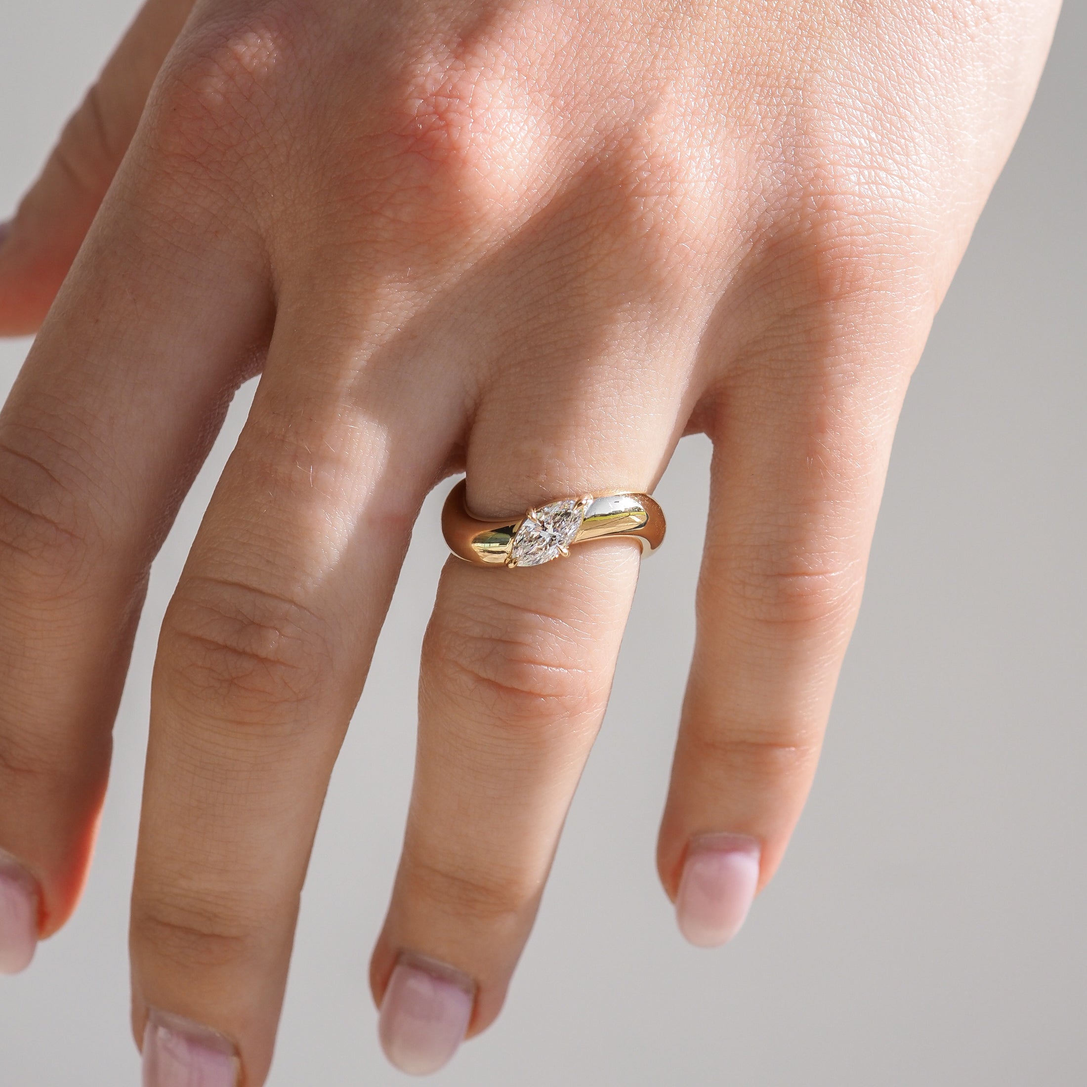 A hand wearing an elegant gold ring with a single, prominent diamond set in the centre, showcasing luxury jewellery design.