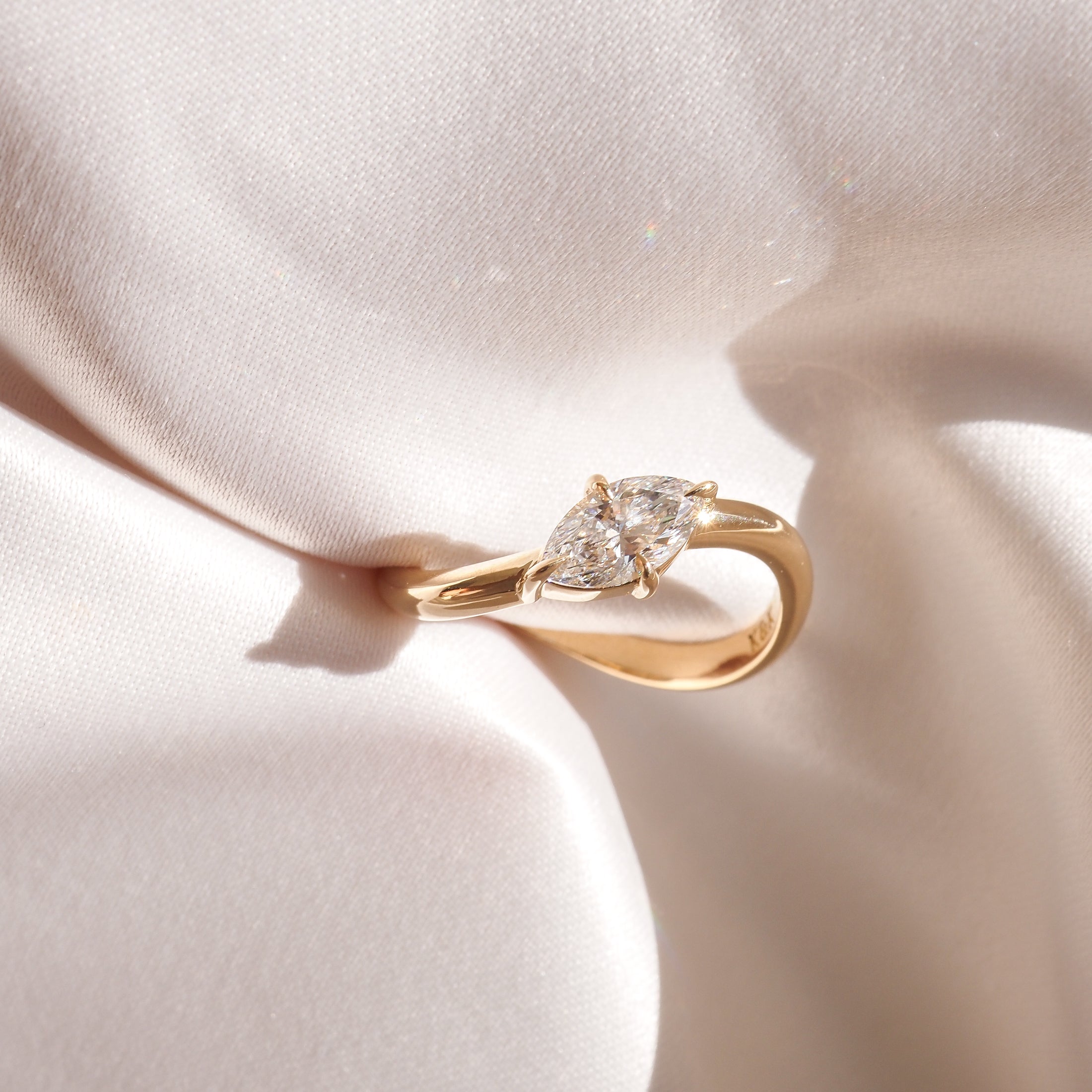 Gold ring with dual pear-shaped diamonds on elegant white satin backdrop, showcasing luxury jewellery's sophistication and elegance.
