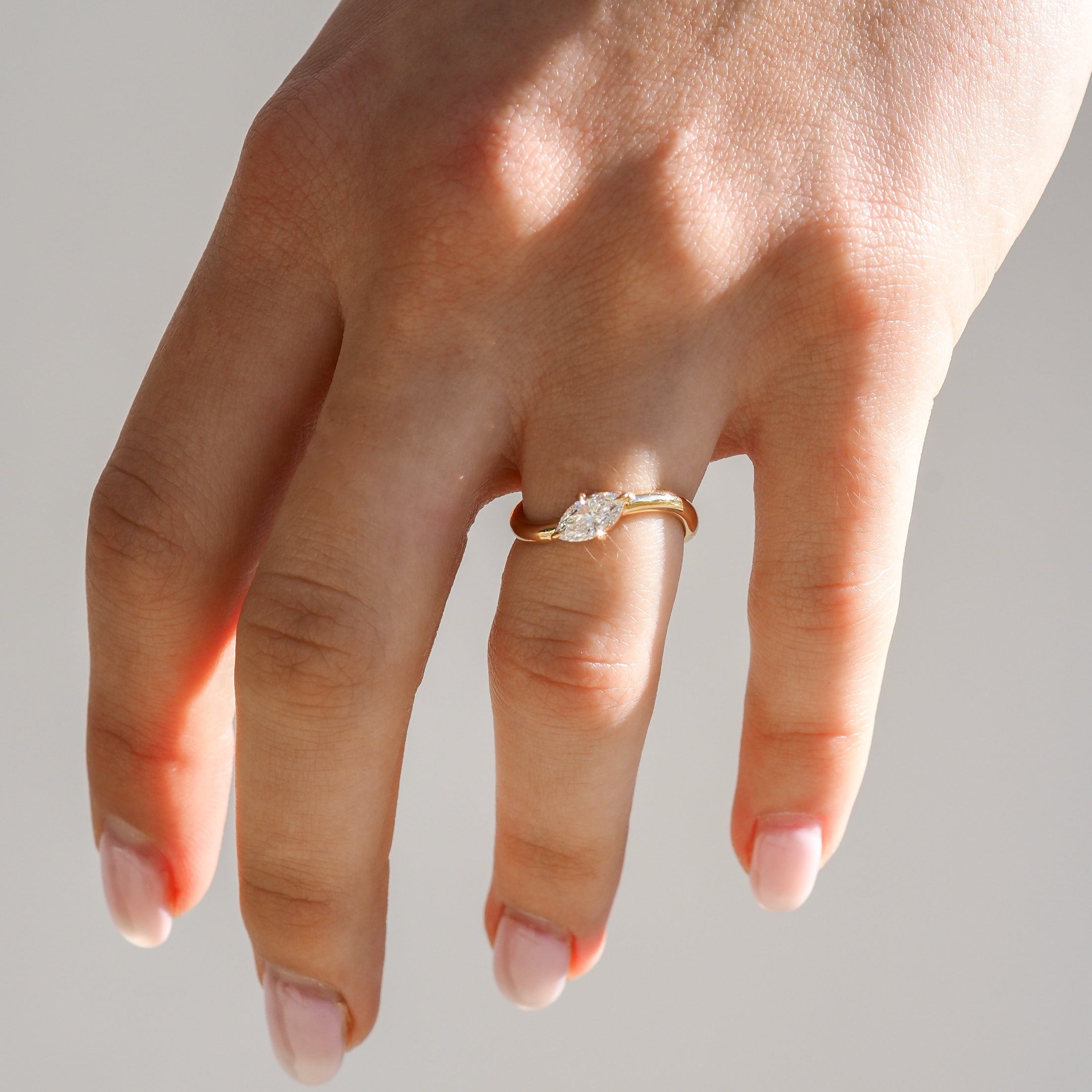 Hand wearing a gold engagement ring with an oval diamond, photographed in natural light against a plain background.