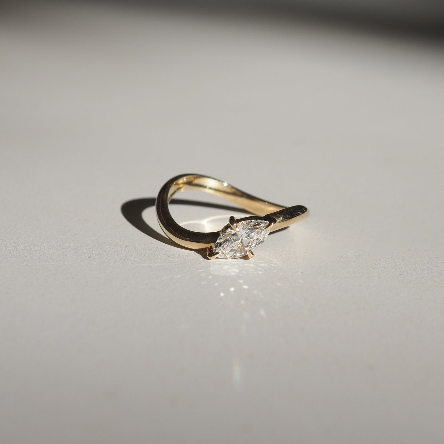 Gold ring with a marquise-cut diamond, elegantly curved band, casting a shadow on a white surface. Perfect for luxury jewellery lovers.