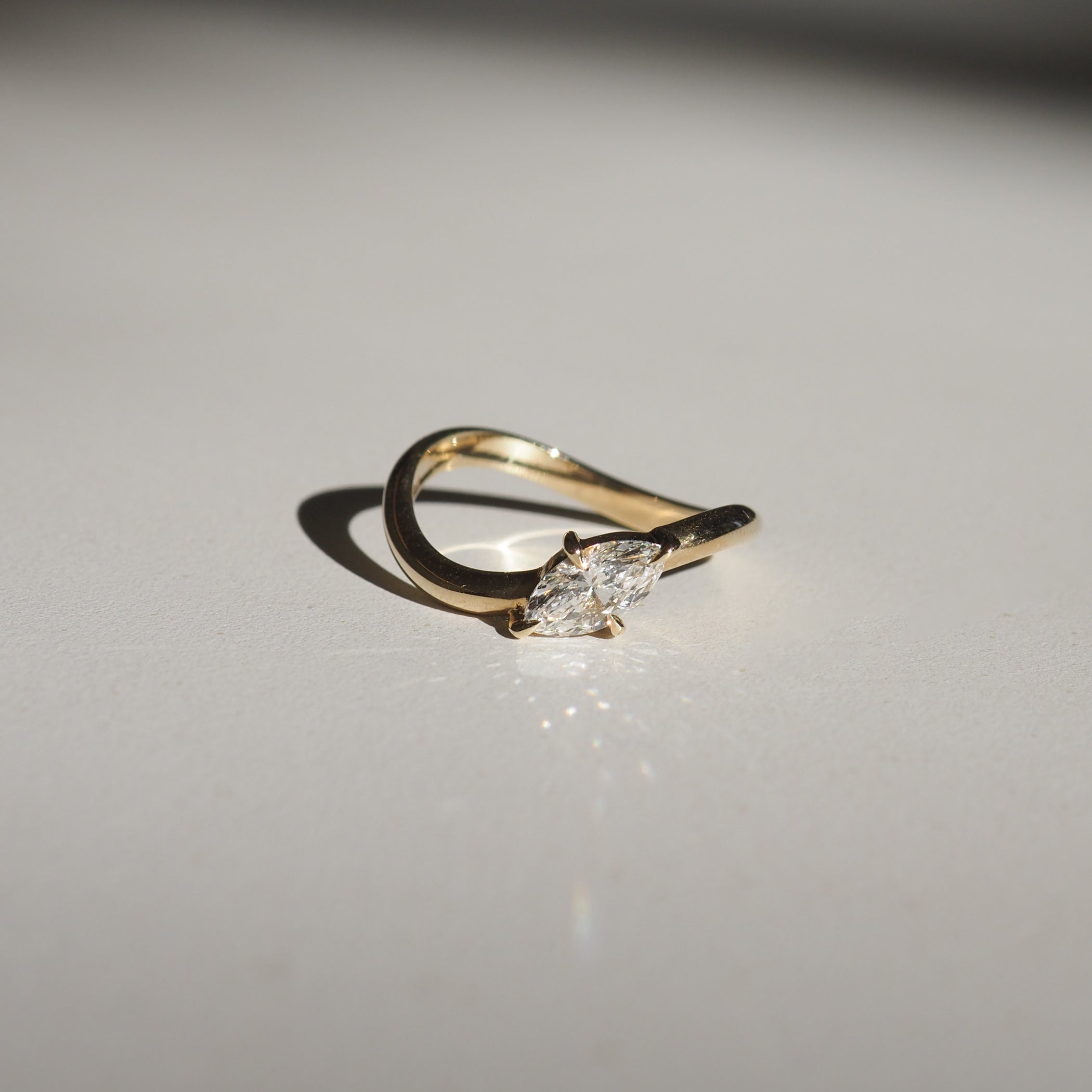 Gold ring with a marquise-cut diamond, elegantly curved band, casting a shadow on a white surface. Perfect for luxury jewellery lovers.
