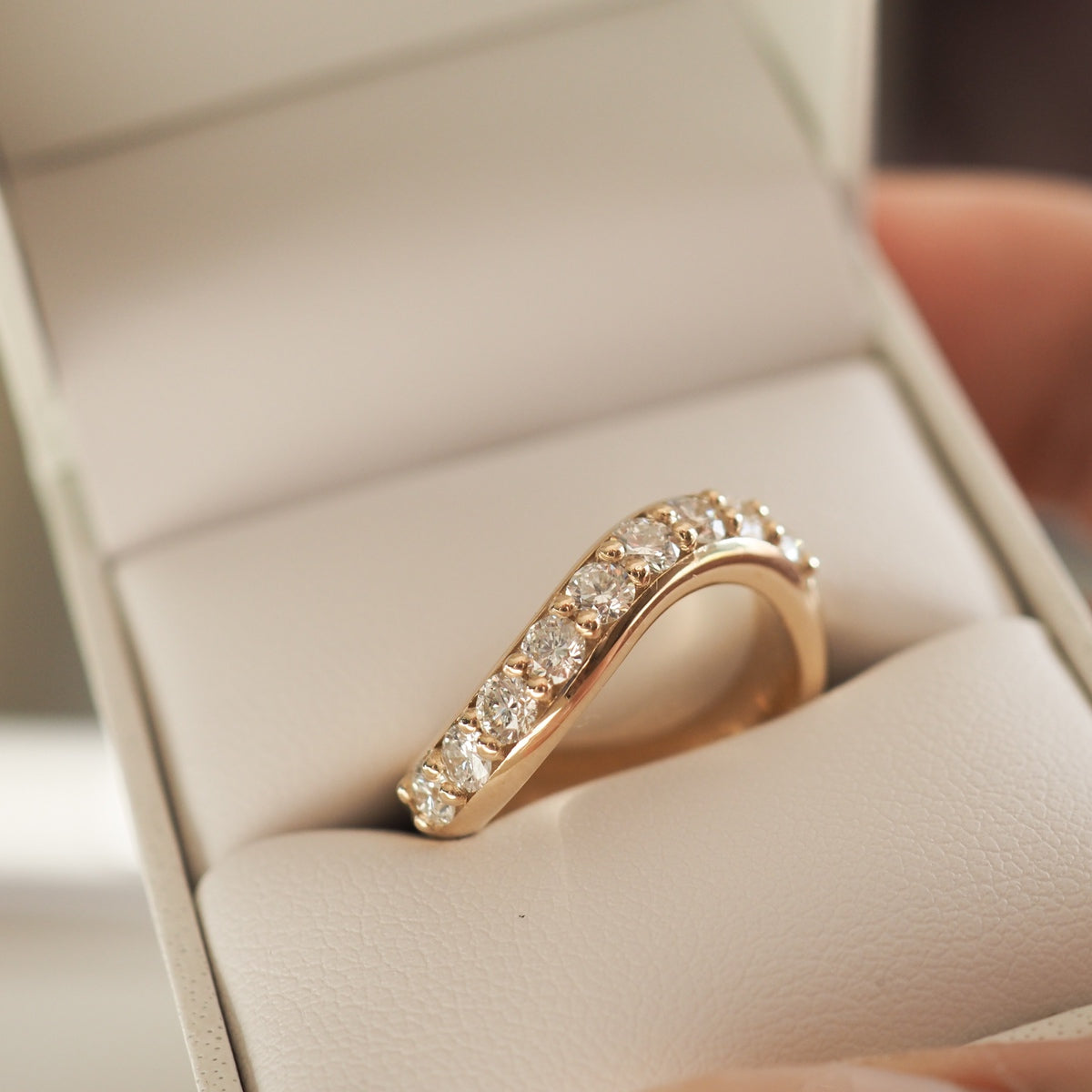 A curved gold ring adorned with sparkling diamonds, elegantly presented in a white jewellery box.