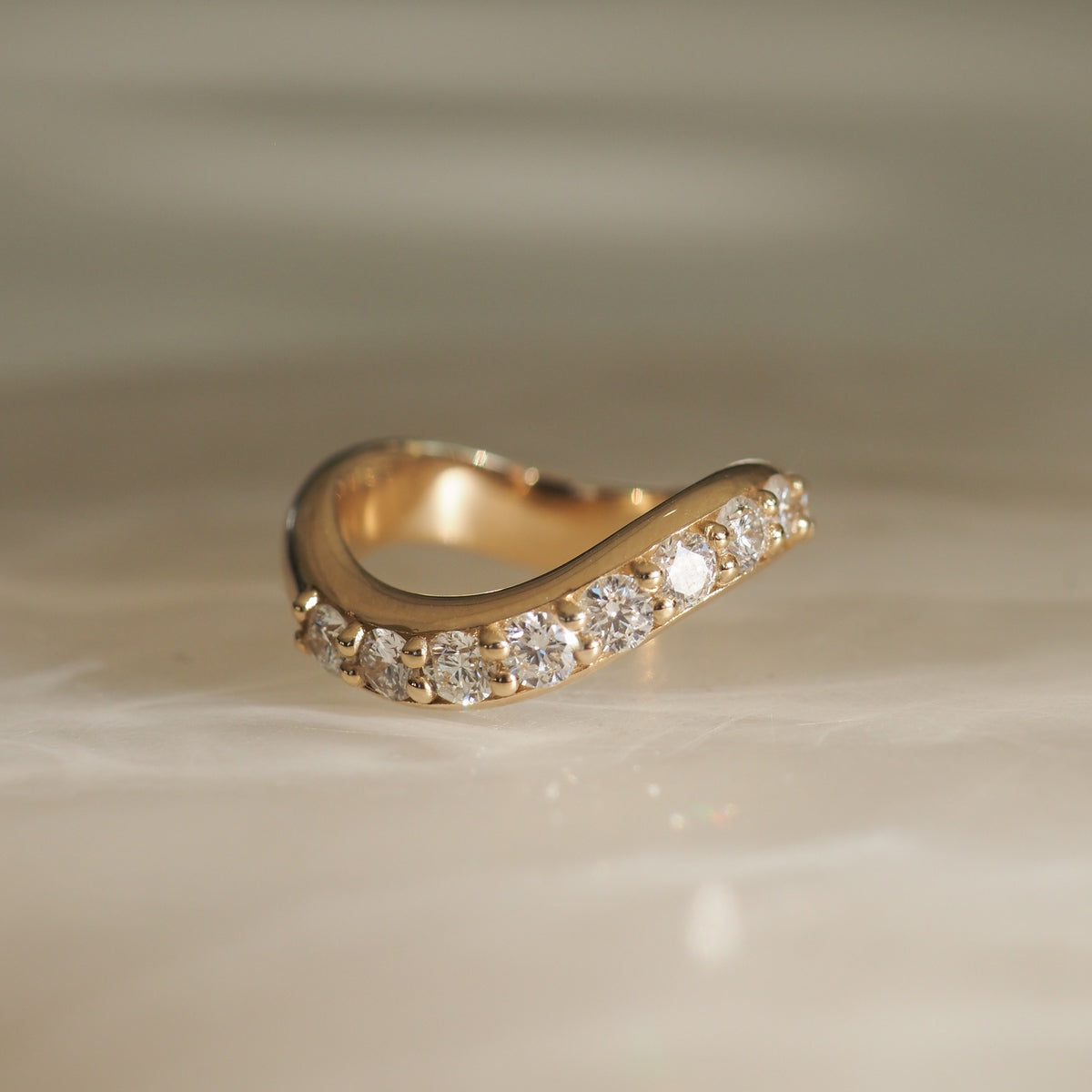 Gold ring studded with sparkling diamonds, elegantly curved design, embodies luxury jewellery and high-end craftsmanship on a soft background.