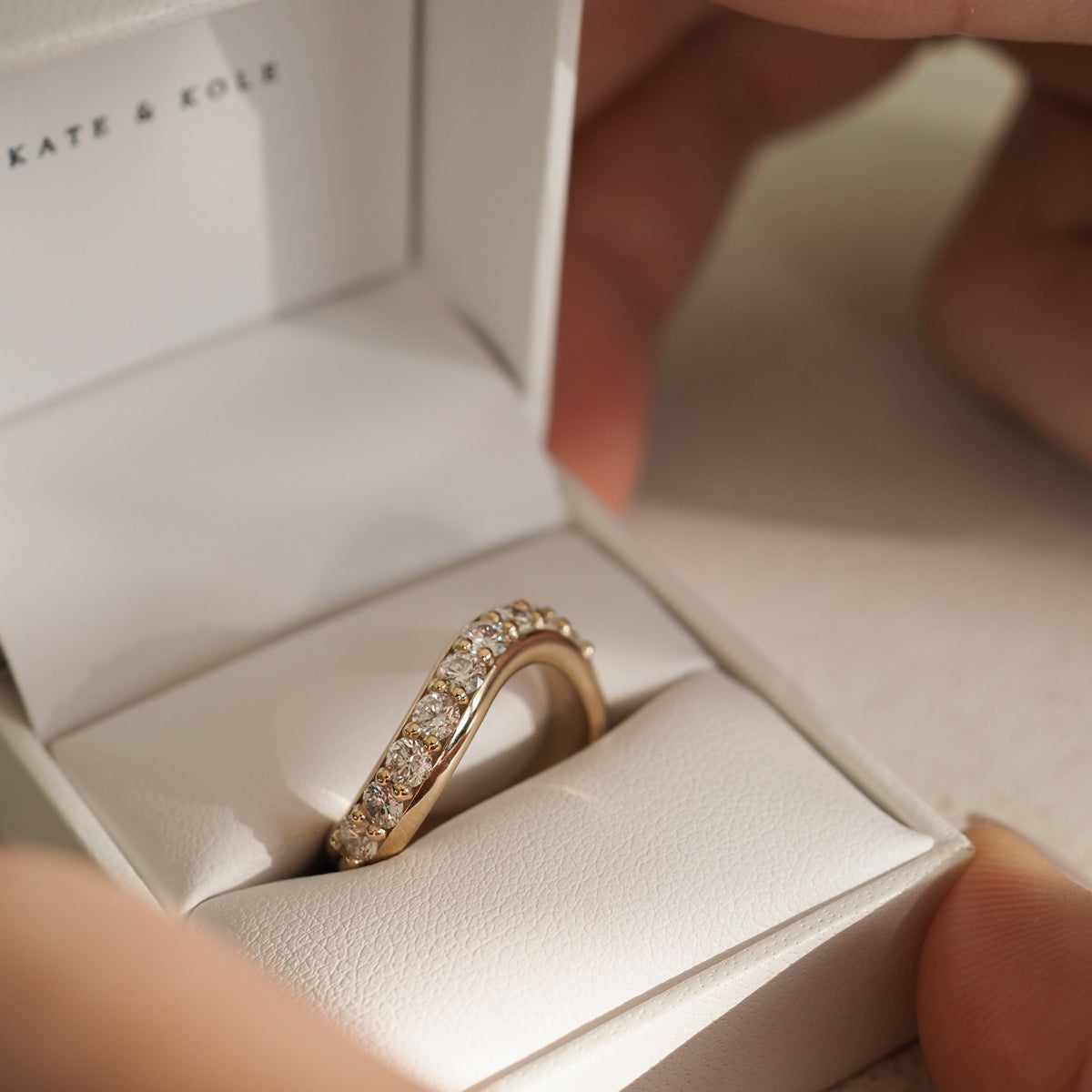 Gold diamond ring with intricate design in a luxurious white jewellery box. Hands opening the box, exuding elegance and opulence.