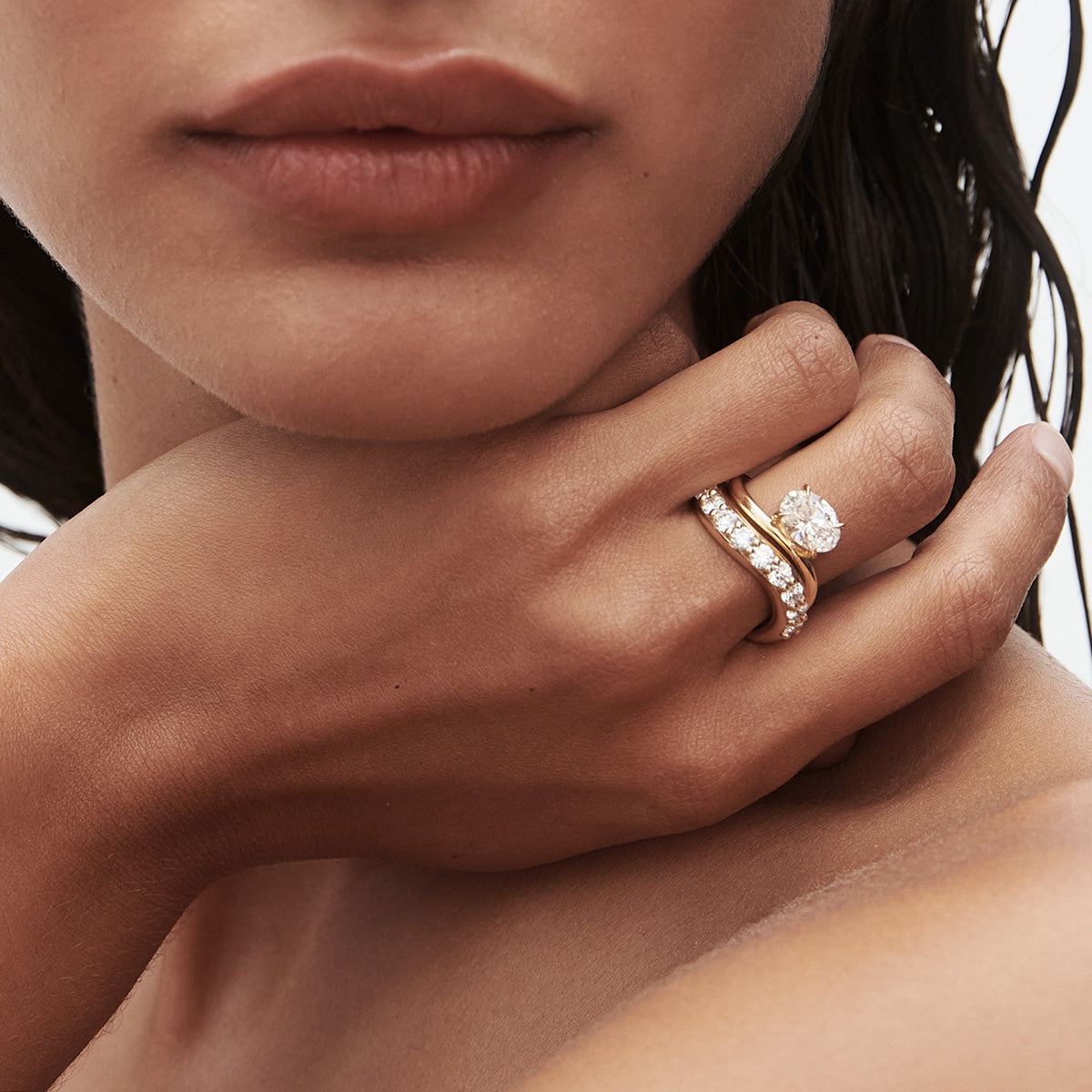 Close-up of a woman's hand adorned with a gold band and diamond ring, showcasing luxury jewellery. She gracefully touches her neck.