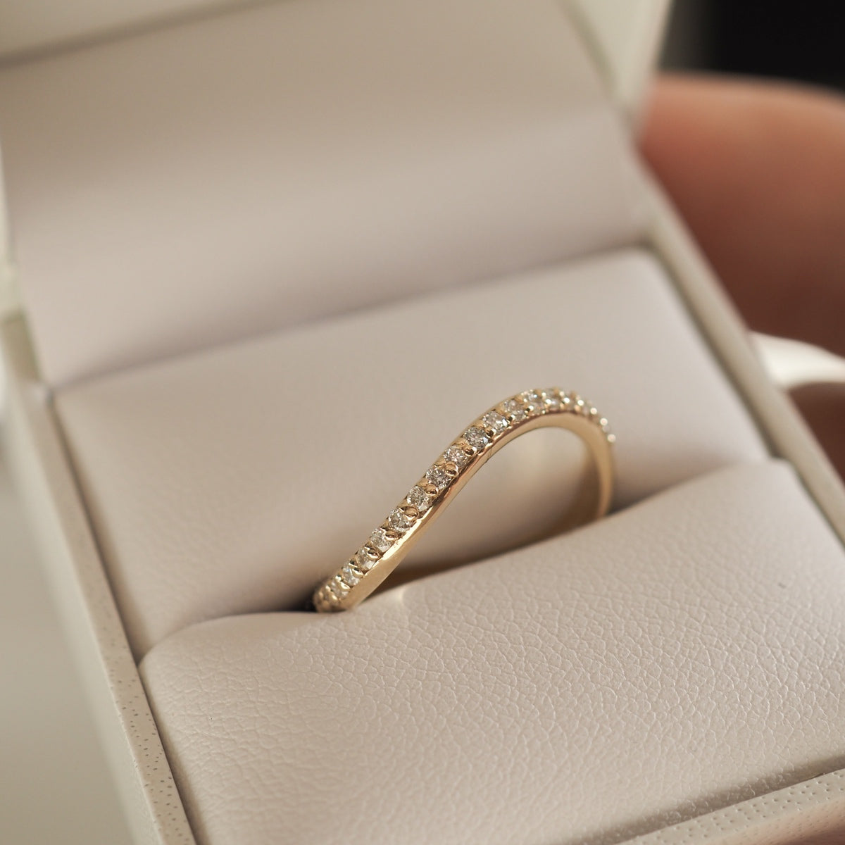 Gold curved wedding band with small diamonds in a beige jewellery box, showcasing luxury jewellery design and elegance.