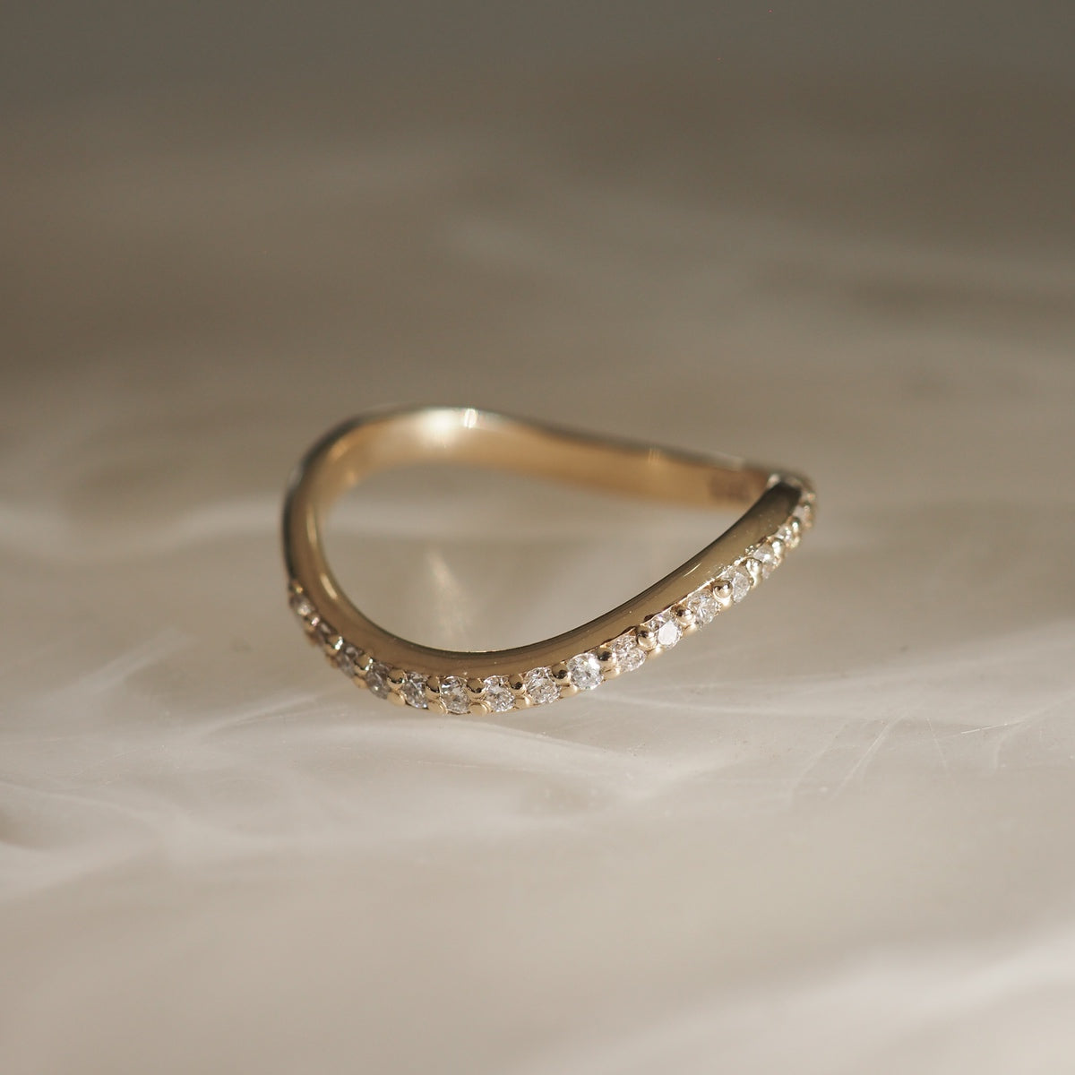 Elegant gold wave ring with sparkling diamonds on a textured beige background. Ideal for luxury jewellery lovers seeking unique designs.