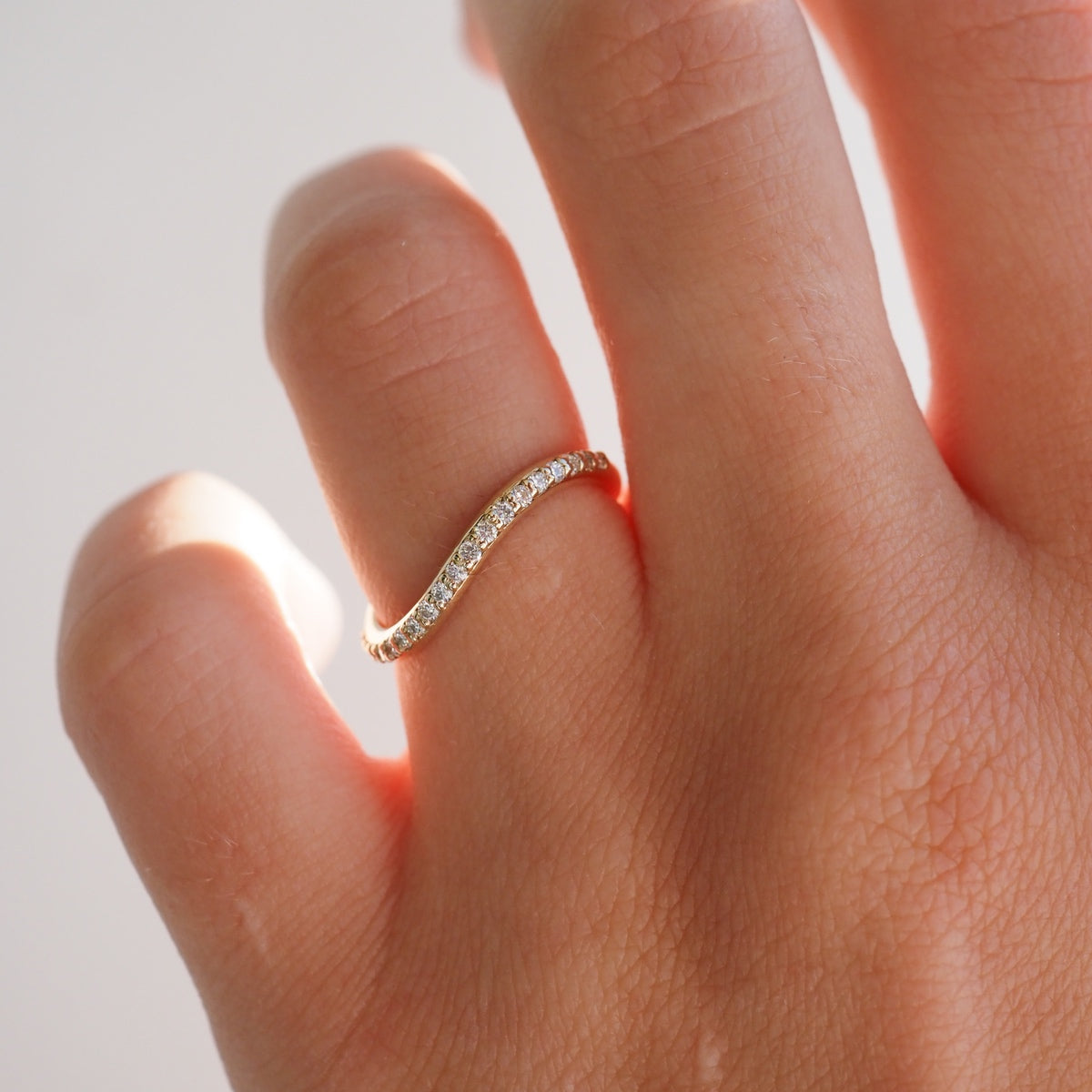Gold diamond eternity ring on finger, luxury jewellery, elegant curved design, close-up, high-end craftsmanship.