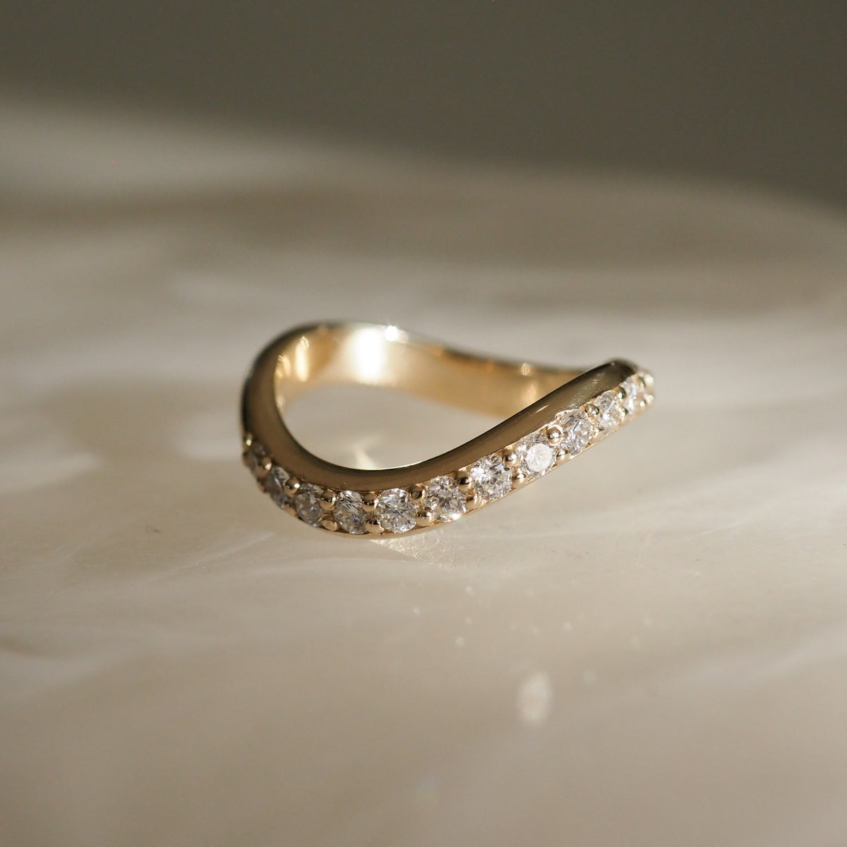 Gold curve ring with diamonds, elegantly designed on soft, illuminated surface. Luxury jewellery piece, reflecting sophistication and grace.