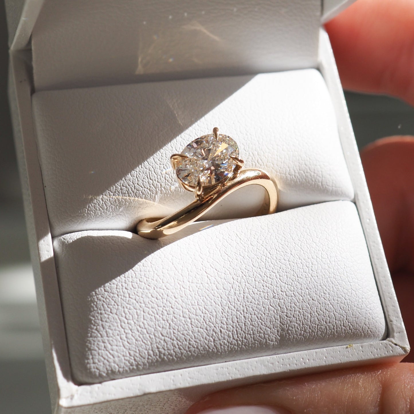 Gold ring with a large diamond in a white jewellery box, displayed in natural sunlight, highlighting its brilliance and elegant design.