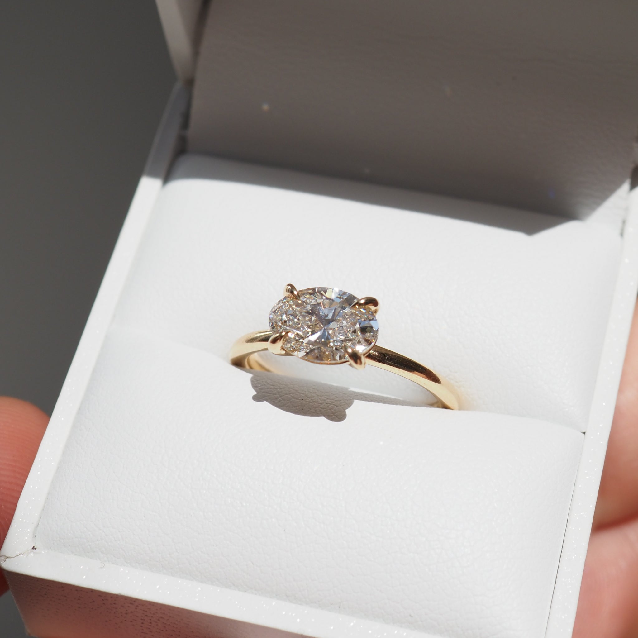 Oval-cut diamond ring set in gold displayed in an open white jewellery box, capturing luxury and elegance.
