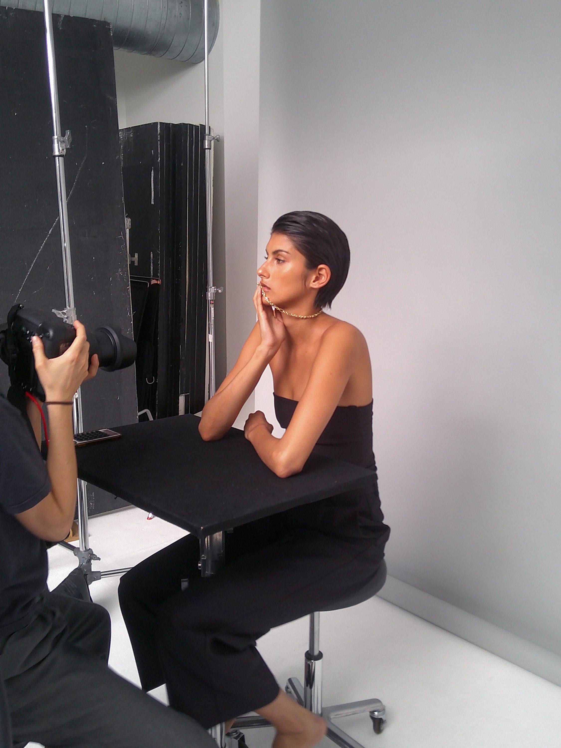 Woman in black strapless outfit poses thoughtfully for a photoshoot, highlighting luxury jewellery, against a minimalist studio backdrop.