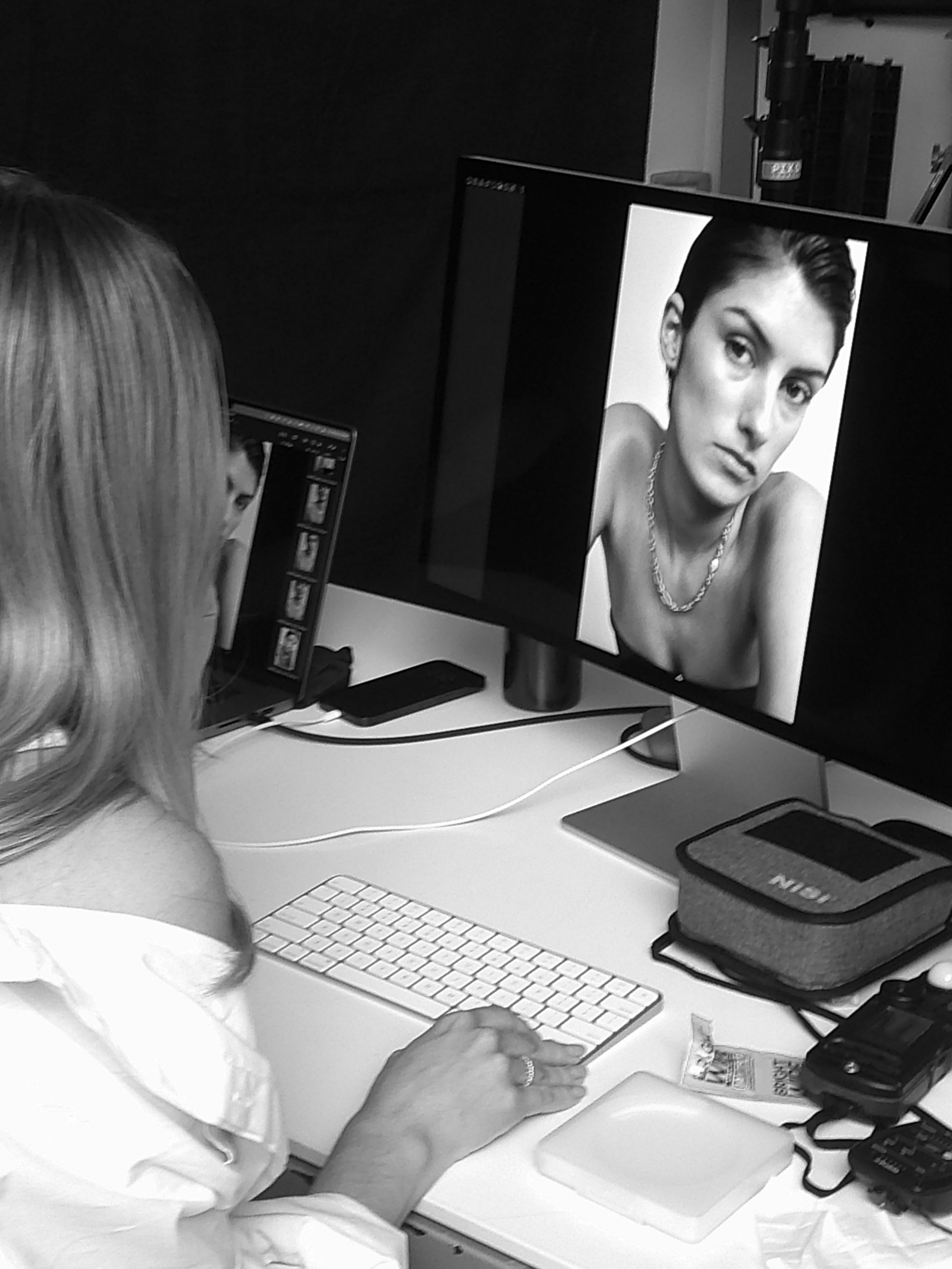 A woman edits a black and white portrait on a computer featuring a model wearing a luxury necklace, capturing a jewellery photoshoot process.