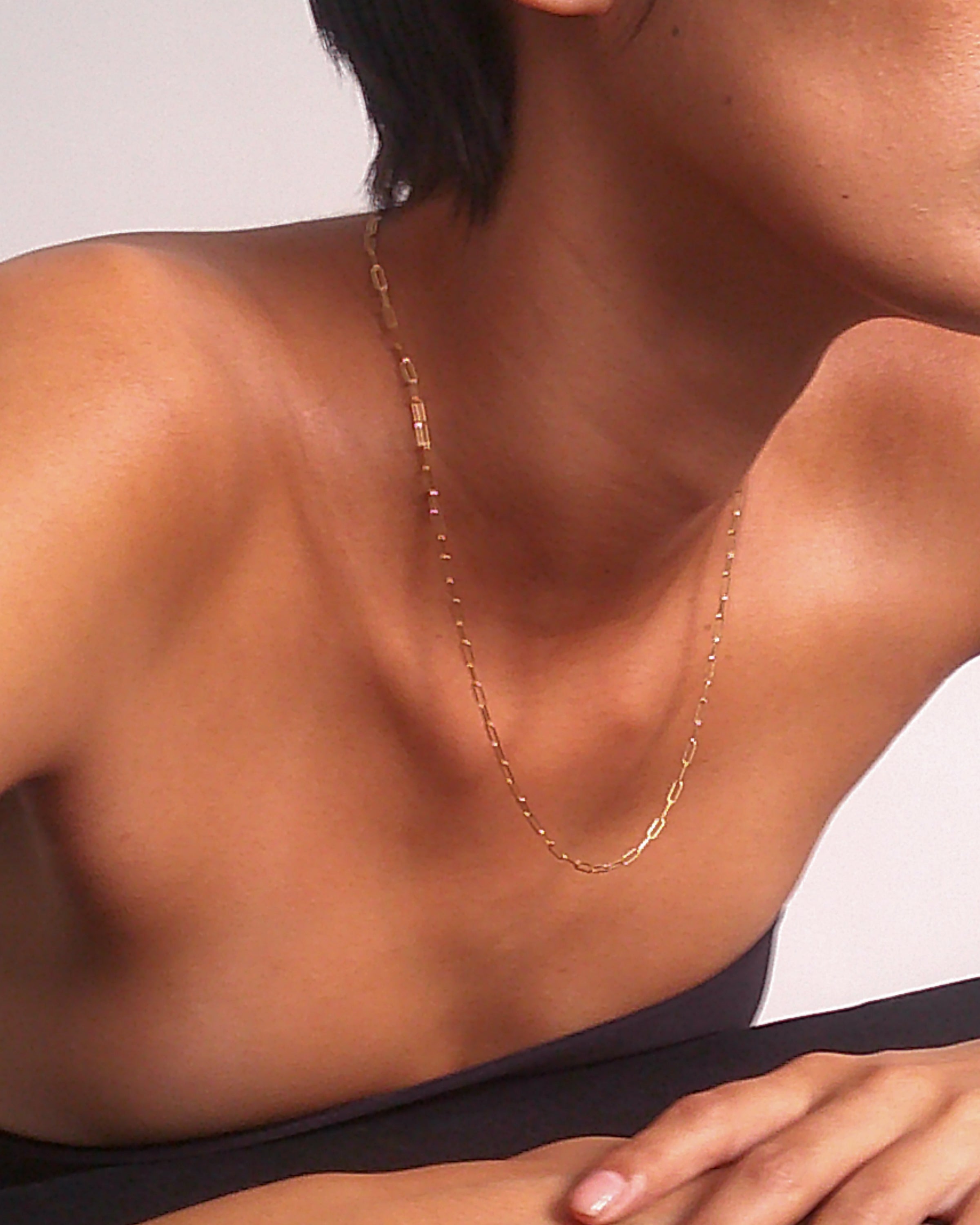 Close-up of a person wearing an elegant gold chain necklace, showcasing luxury jewellery against their bare shoulders and simple backdrop.