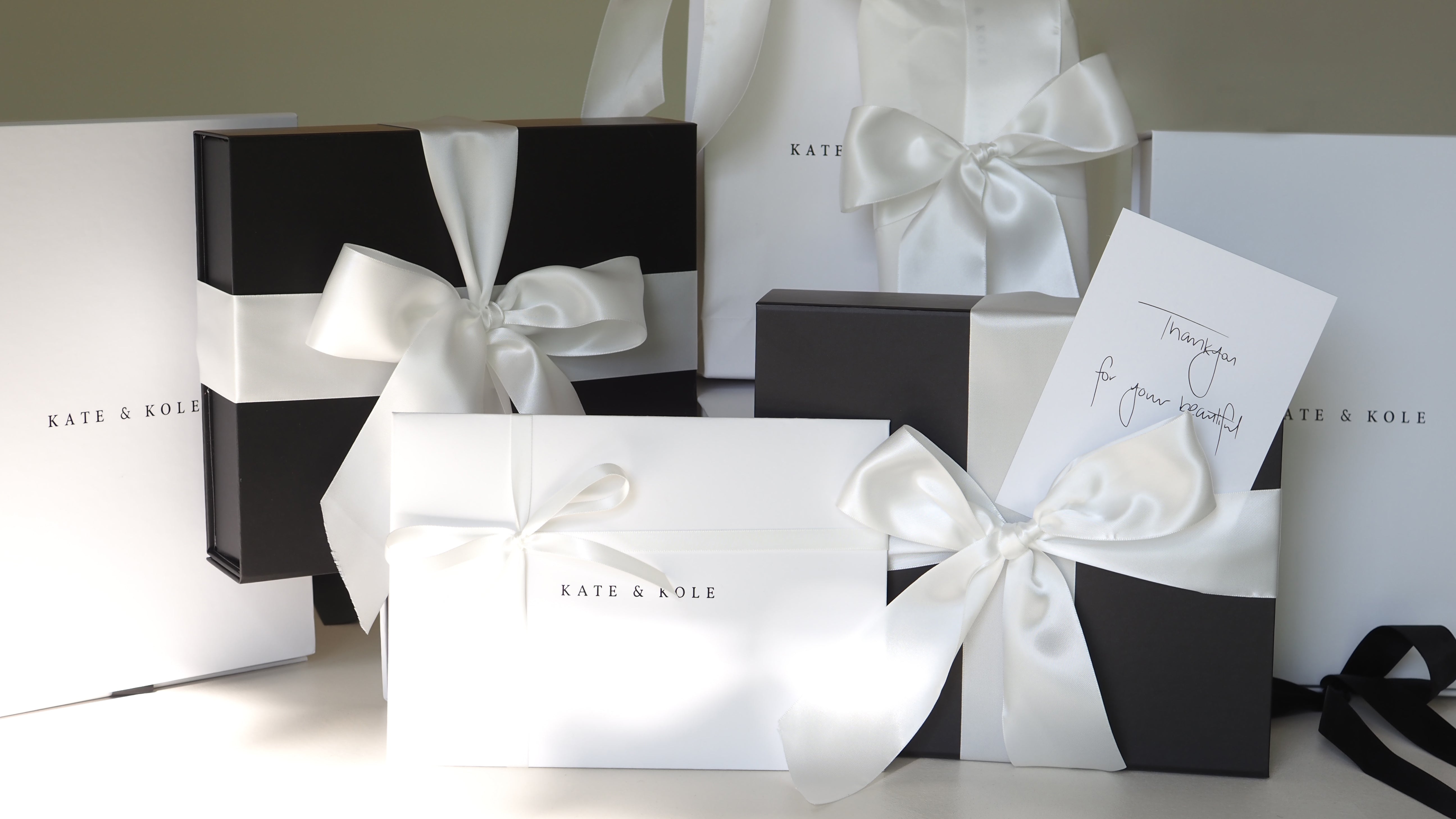 Elegant gift boxes with white satin ribbons from Kate & Kole, featuring a "Thank you for your purchase" note.