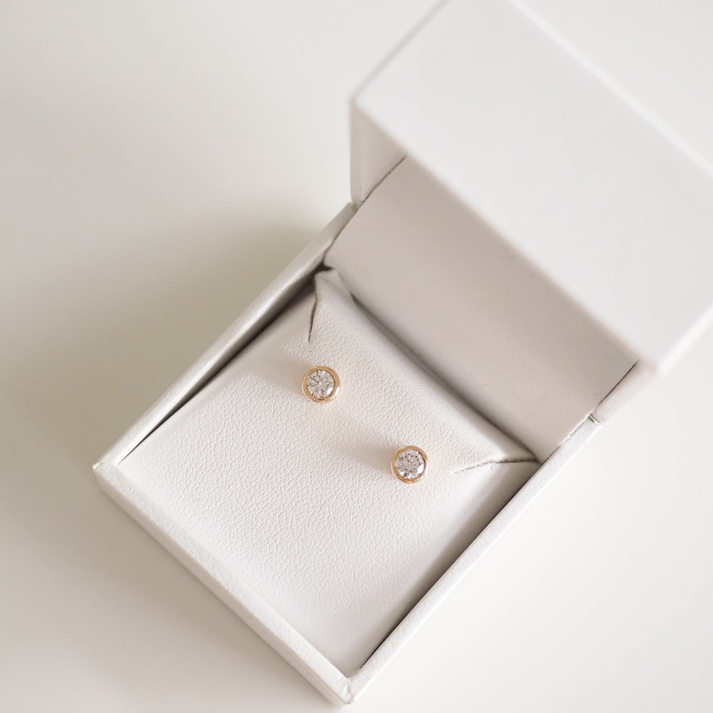 Gold stud earrings with sparkling diamonds in an elegant white jewellery box. Perfect for luxury and sophistication.