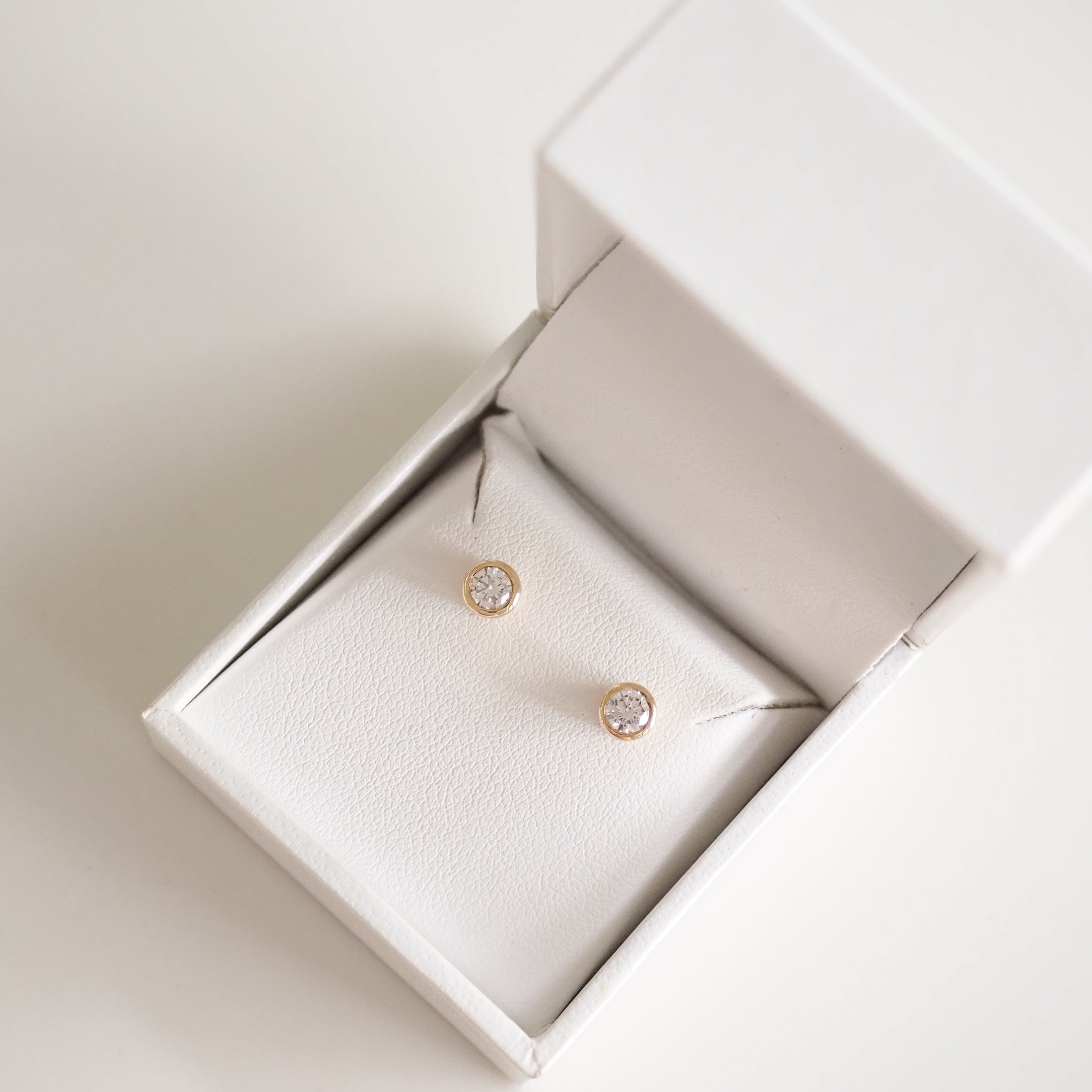 Gold stud earrings with sparkling diamonds in an elegant white jewellery box. Perfect for luxury and sophistication.