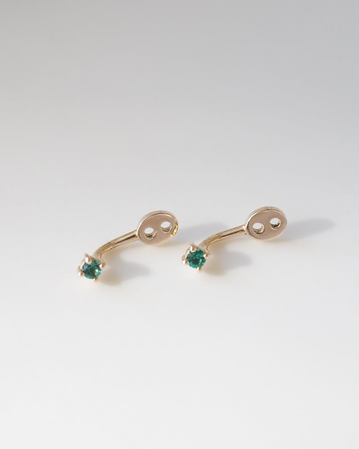 Pair of gold earring jackets with green gemstones on a light gray background