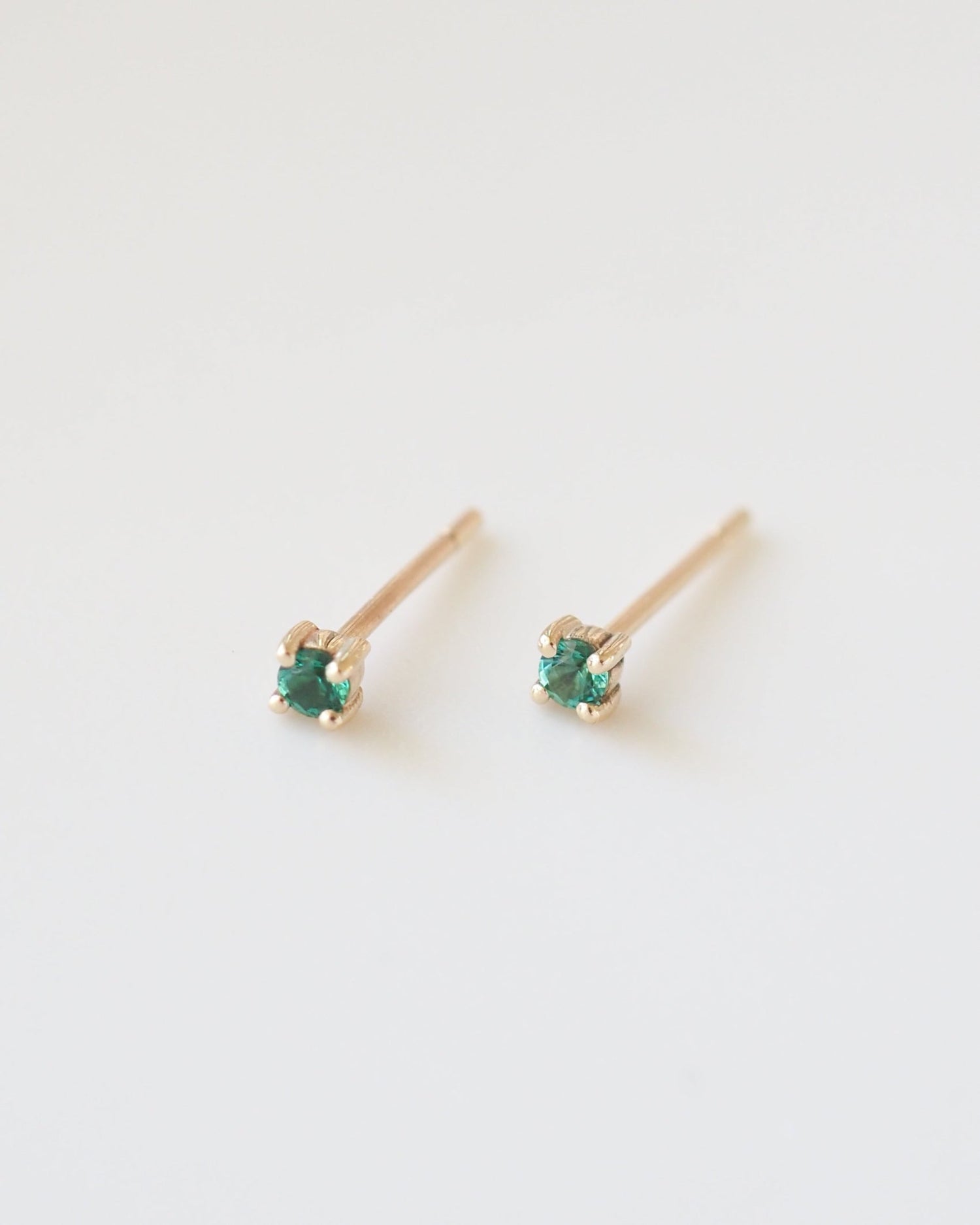Pair of gold earrings with green gemstones on a white background