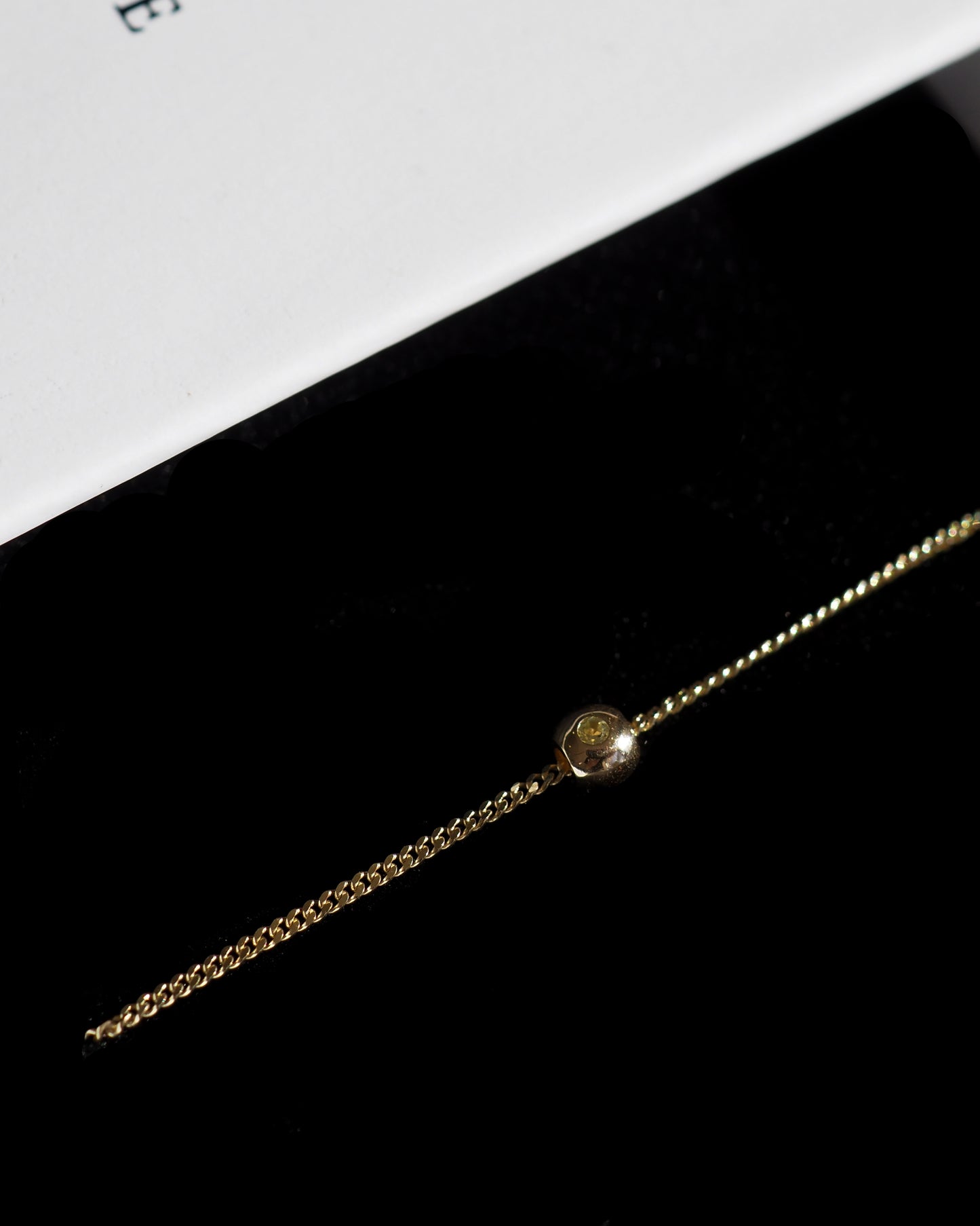 Gold chain bracelet with a single gemstone, elegantly displayed on black velvet with a white card. Perfect for luxury jewellery enthusiasts.