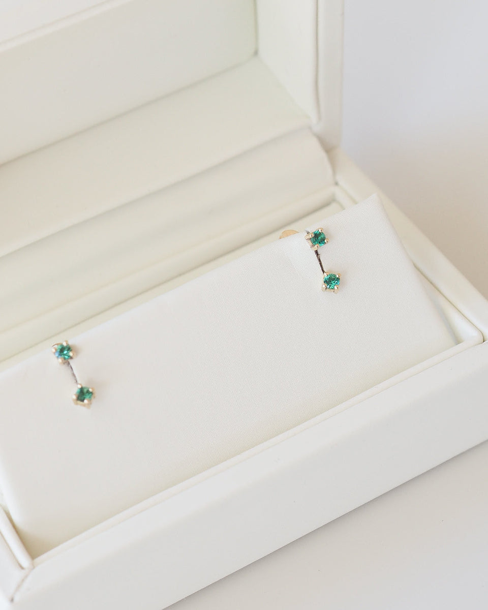 Pair of earrings with green gemstones in a white jewelry box