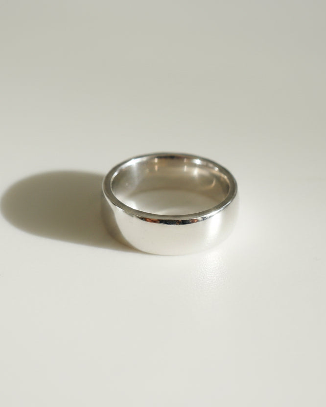 Gold band ring on white surface, casting a subtle shadow. Elegant and timeless design, reflecting high-end jewellery craftsmanship.