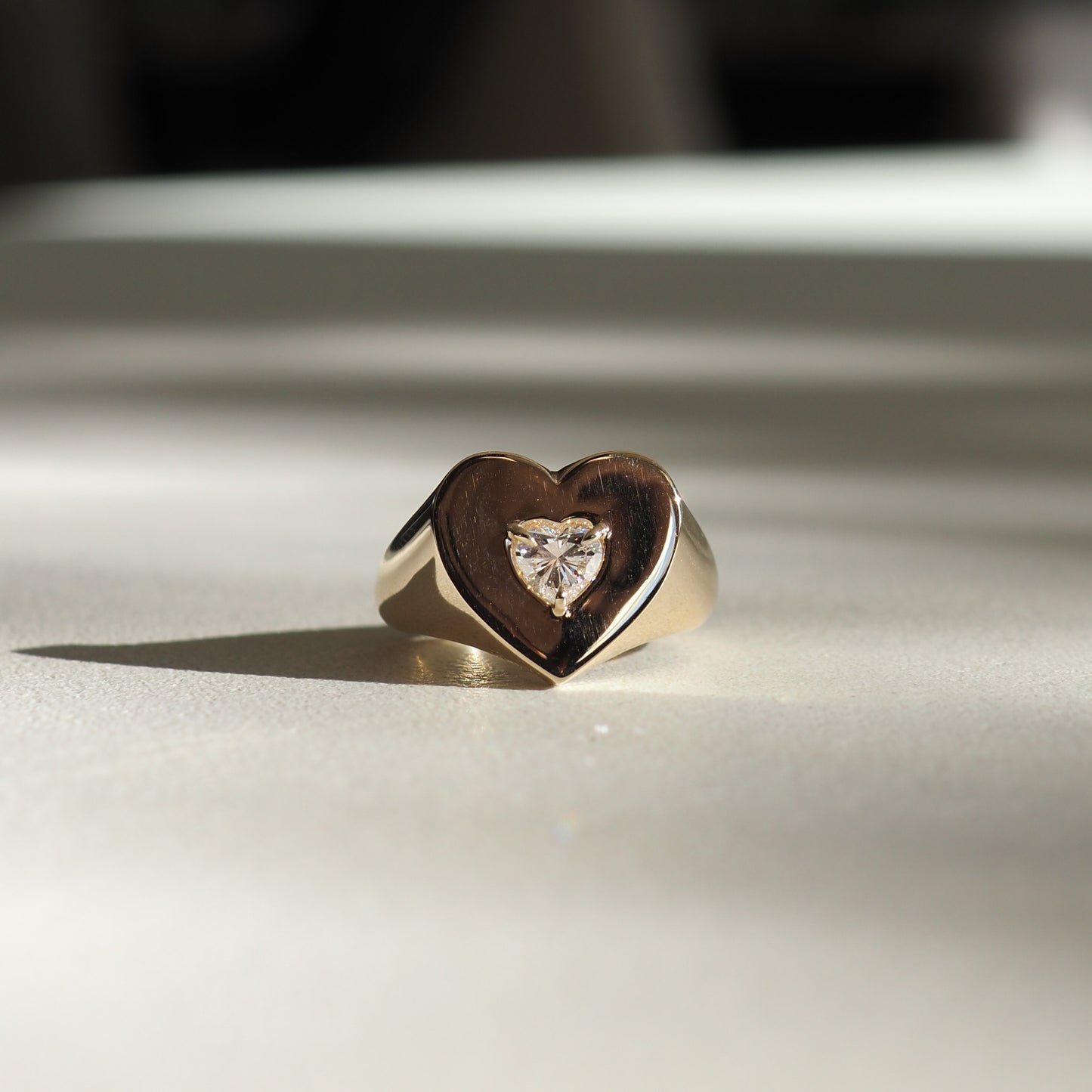 Gold heart-shaped ring with central diamond detail, elegantly positioned on a light surface, reflecting luxury jewellery style.