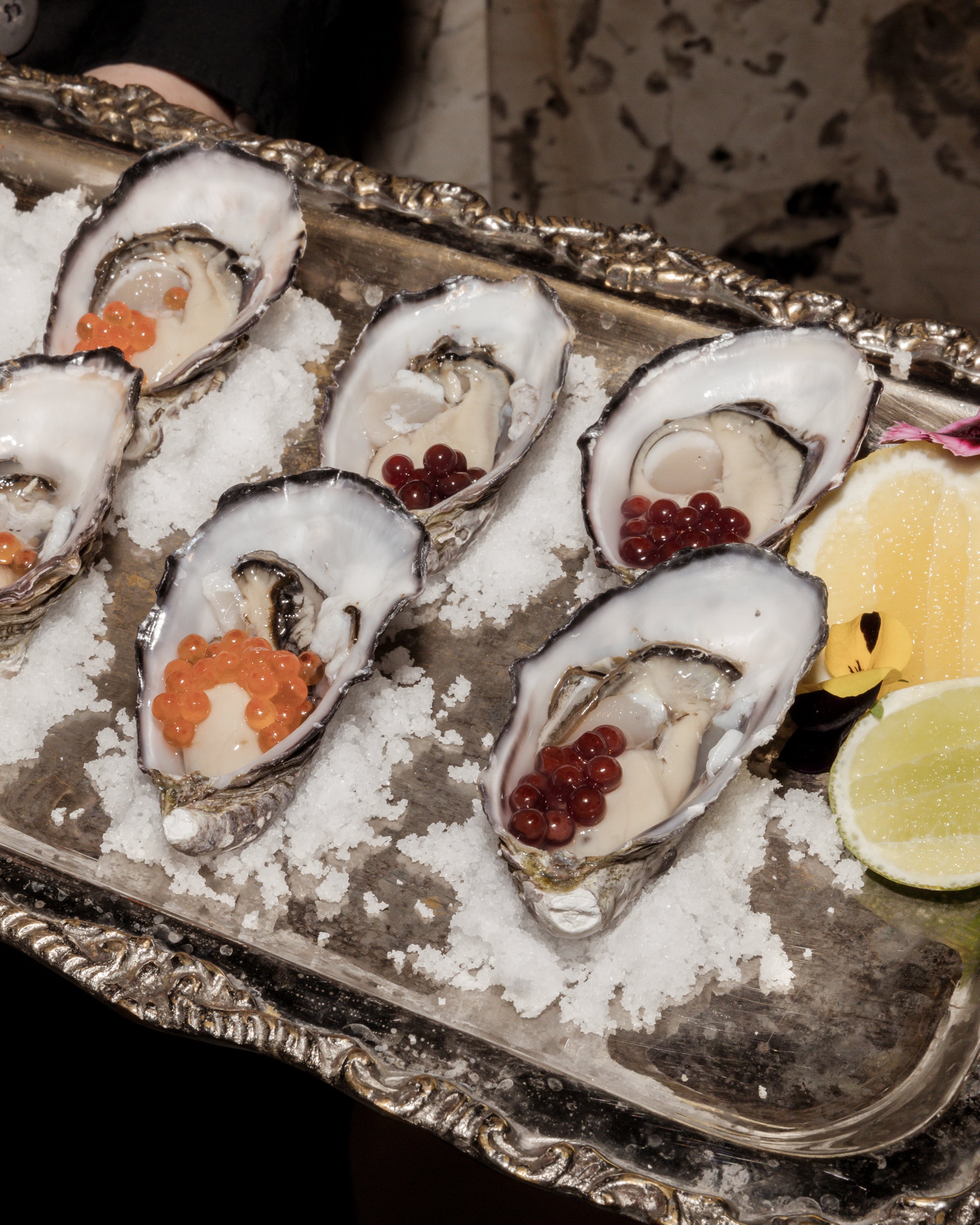 Elegant tray of oysters garnished with red and orange pearls, served on a bed of ice with lemon and lime wedges, embodying luxury dining.
