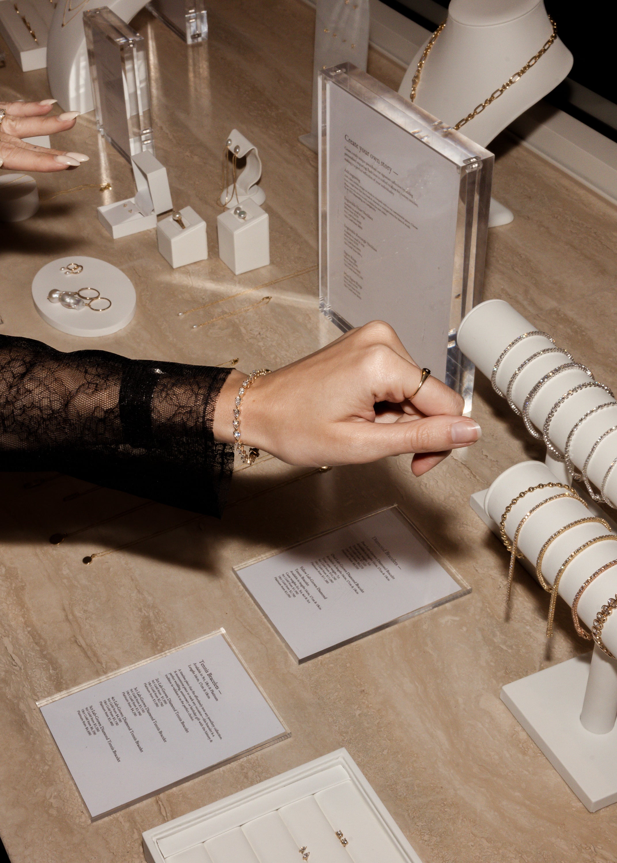 Luxurious jewellery display with bracelets, necklaces, and earrings on a marble countertop. A hand models a delicate bracelet.