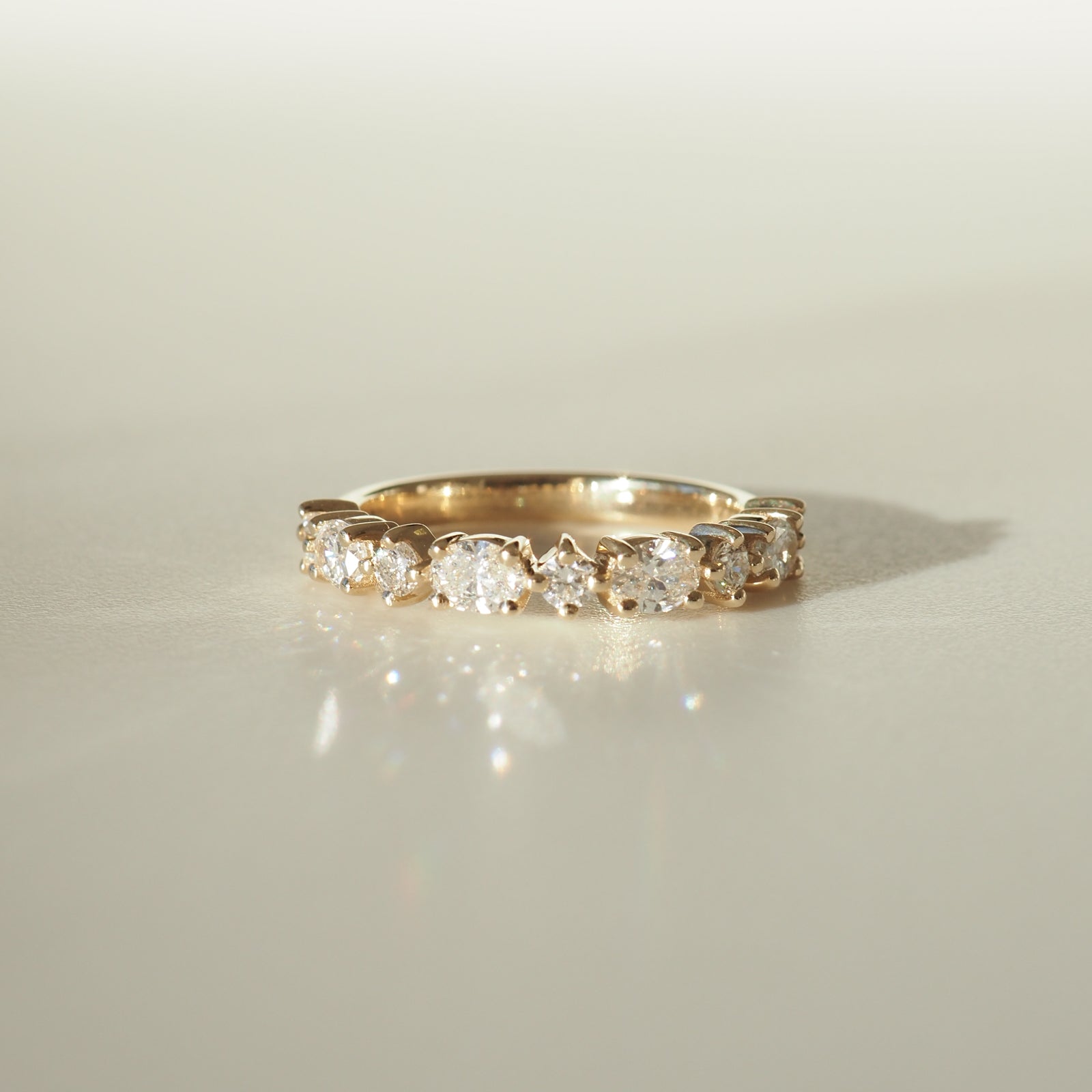 Gold ring with oval-cut diamonds set in a half eternity band. The ring sparkles elegantly against a soft, neutral background.