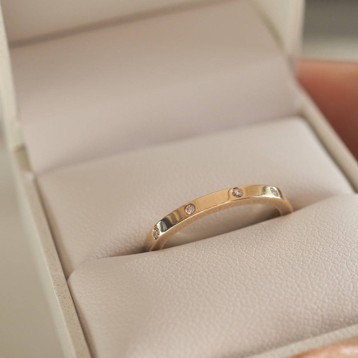 Gold band ring with small diamonds, displayed in a beige jewellery box. Elegant and luxurious design, perfect for a sophisticated style.