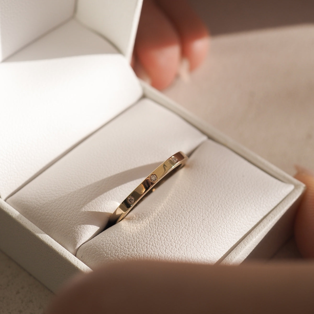 Gold ring with small diamonds in a white leather jewellery box, bathed in soft sunlight, suggesting luxury and elegance.