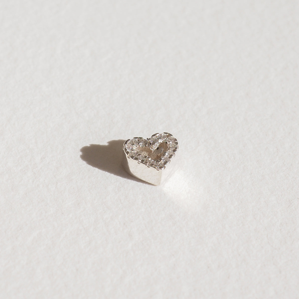 Heart-shaped diamond stud earring on white surface, luxury jewellery, sparkling stones, elegant design.