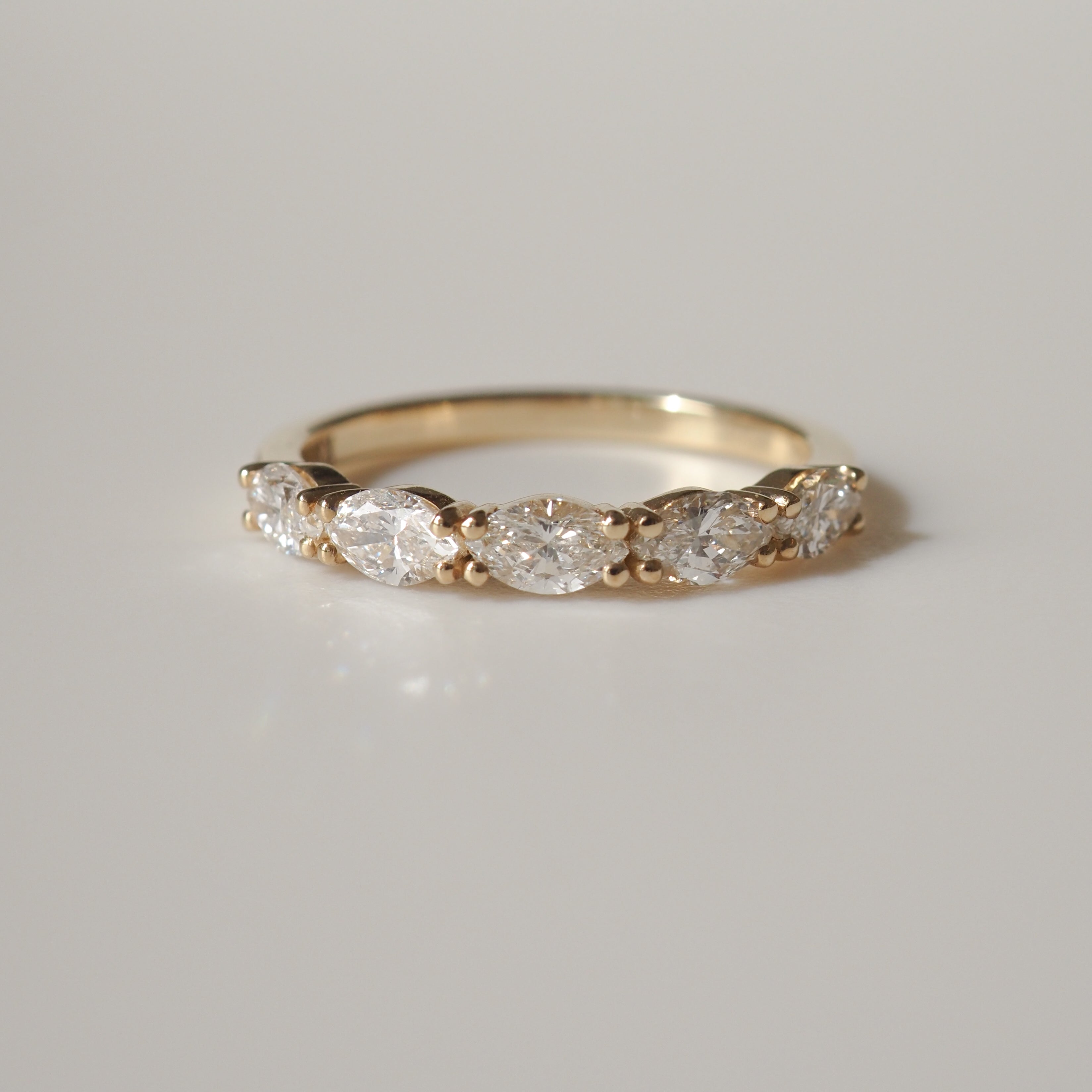 Gold ring with marquise-cut diamonds in an elegant row, reflecting light against a plain background. Perfect luxury jewellery piece.