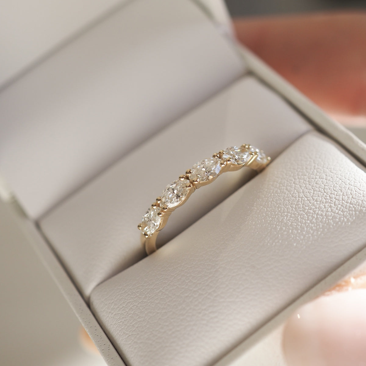 Elegant gold ring with five sparkling diamonds in a cream jewellery box, showcasing luxury craftsmanship and timeless design.